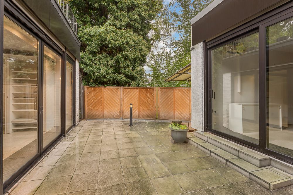 Geflieste Terrasse mit Pflanzkübel, Holzzaun und großen Glasschiebetüren.