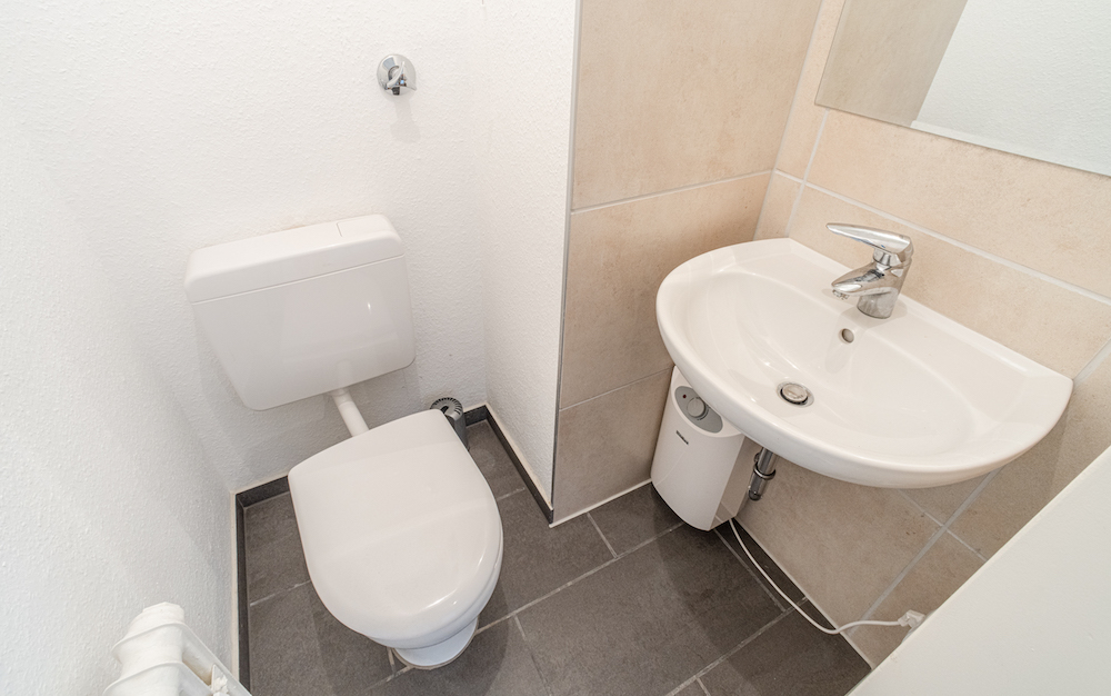 Kleines Badezimmer mit Toilette, Waschbecken und Spiegel an der Wand.