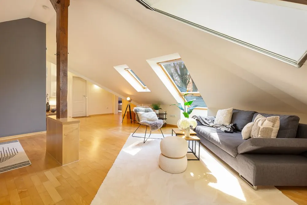 Helles Wohnzimmer im Dachgeschoss mit Sofa, Teppich, Sesseln und großen Dachfenstern.