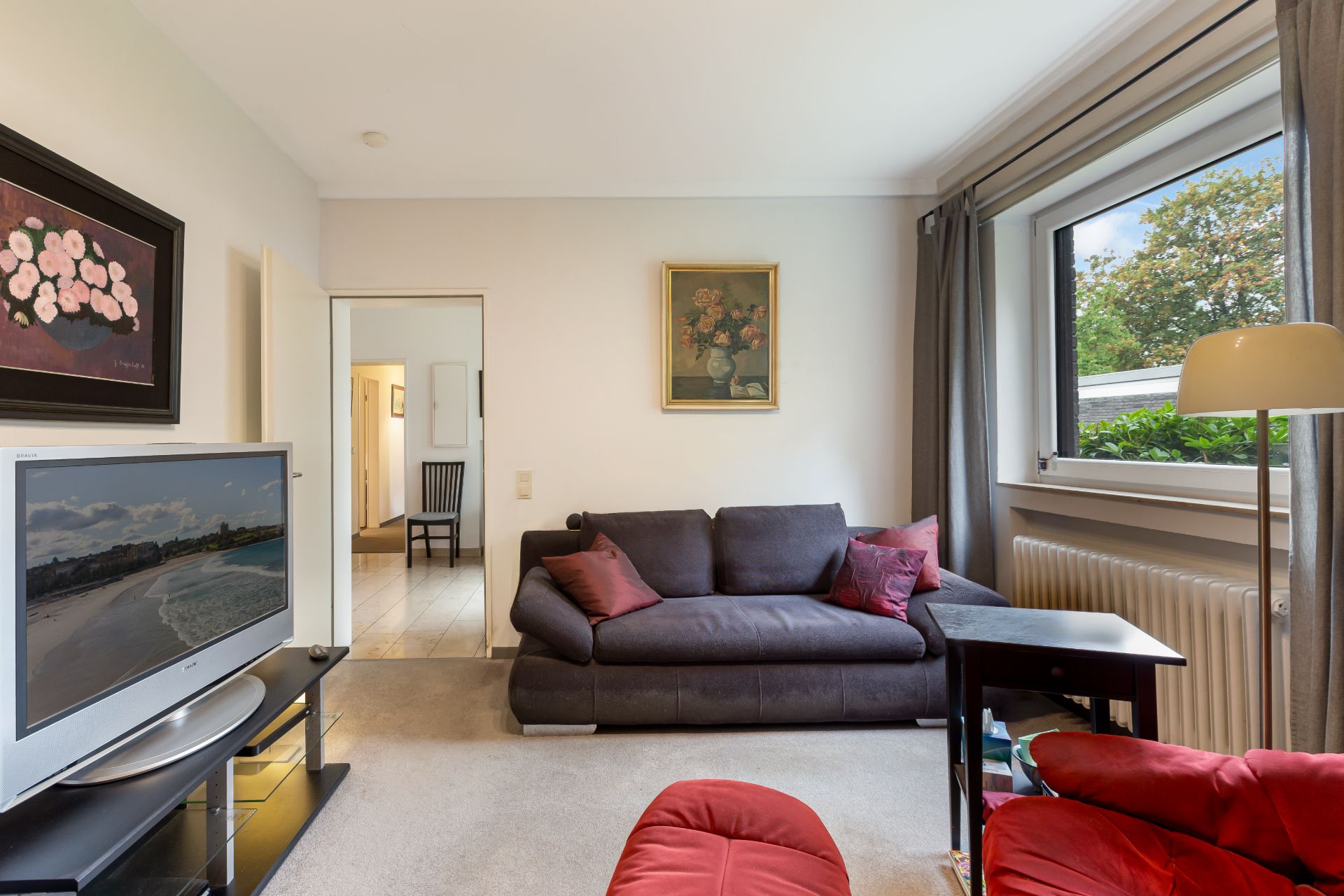 Wohnzimmer mit grauem Sofa, Fernseher, großem Fenster und Bildern an der Wand.