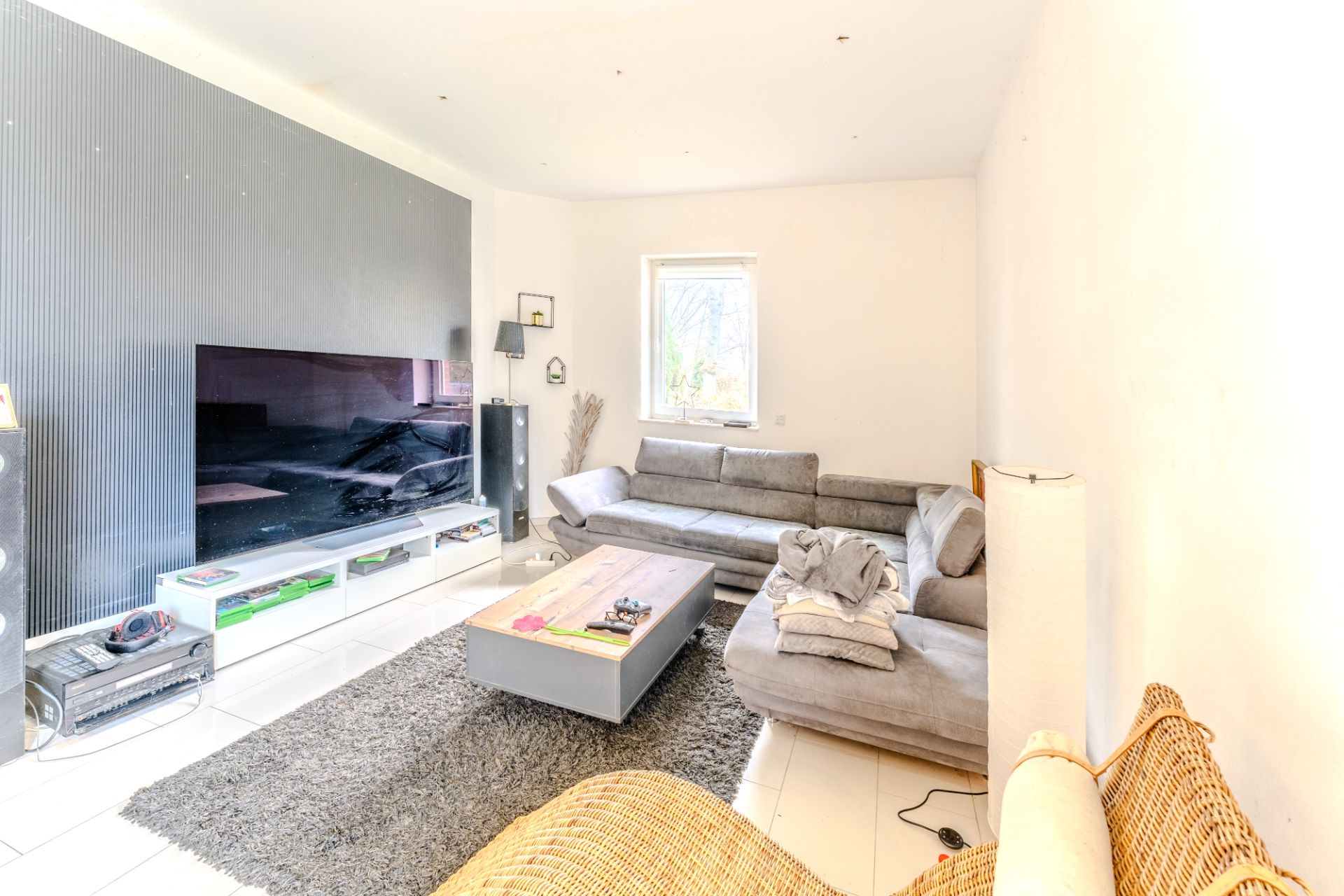 Helles Wohnzimmer mit grauem Ecksofa, niedrigem Couchtisch, Teppich und großem Fernseher.