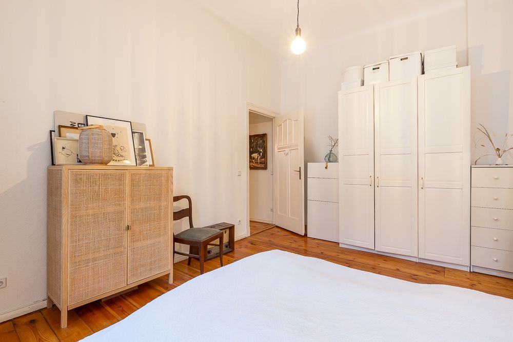 Helles Schlafzimmer mit weißem Kleiderschrank, Holzschrank, Stuhl und Holzboden.