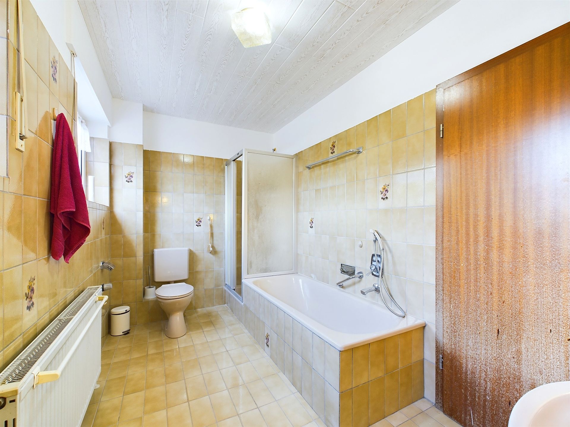 Badezimmer mit gelben Fliesen, Badewanne, Toilette, Dusche und einem Fenster.