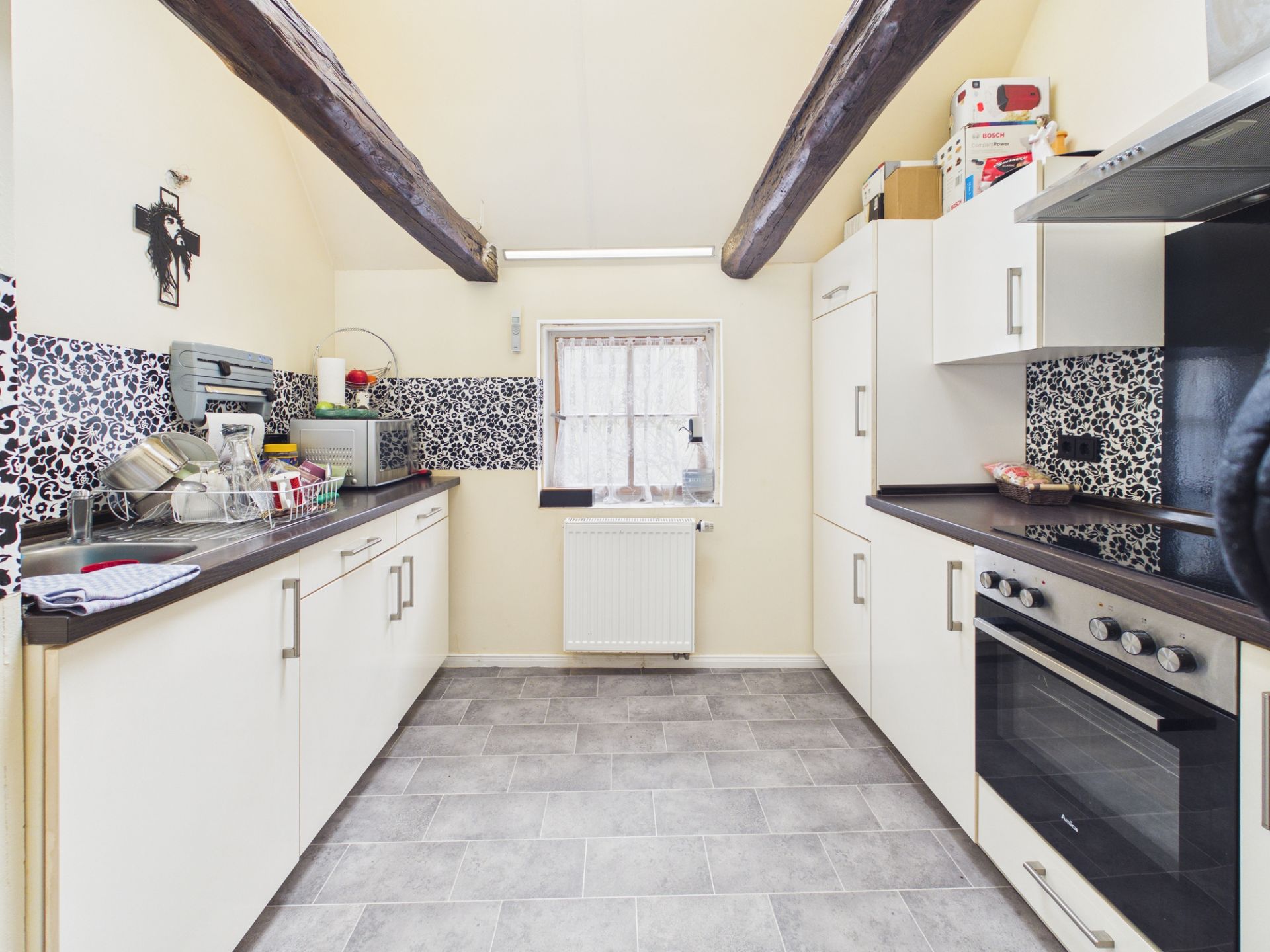 Moderne Küche mit weißen Schränken, dunklen Arbeitsplatten und sichtbaren Holzbalken an der Decke.