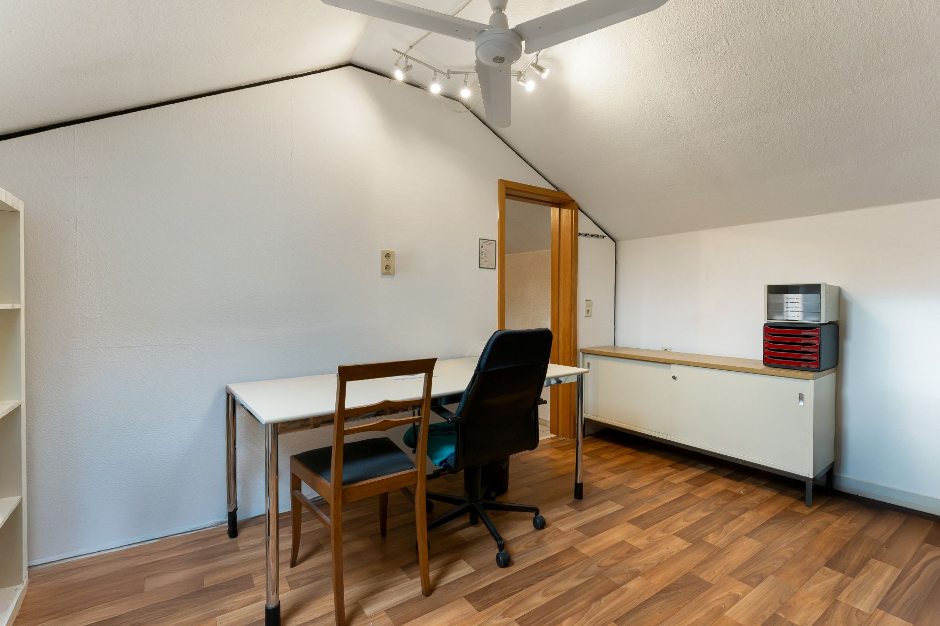Arbeitszimmer mit zwei Stühlen, Schreibtisch, Regal und Sideboard unter Dachschräge.