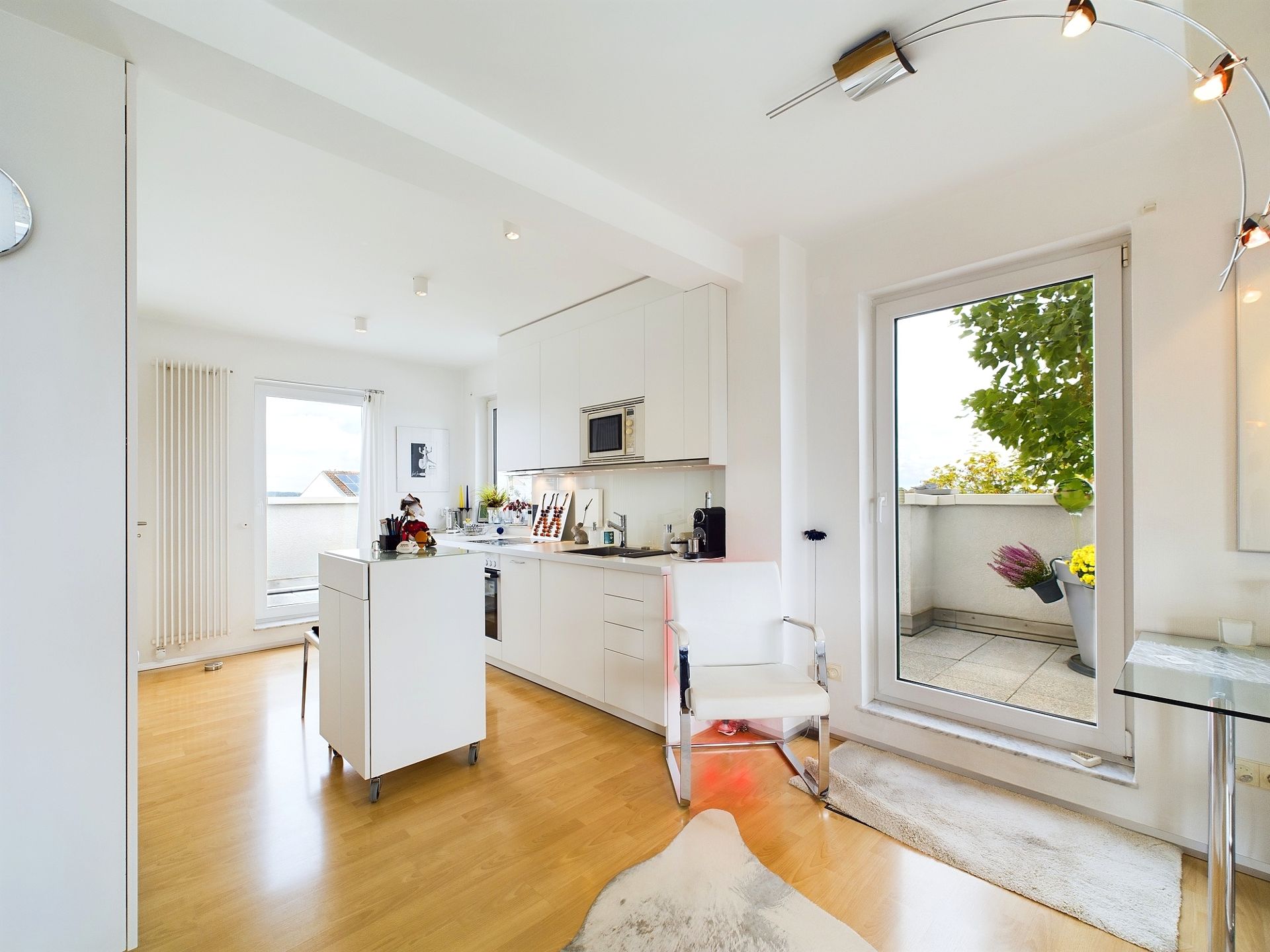 Helle Küche mit weißen Möbeln, Holzfußboden und Zugang zu einem Balkon mit Pflanzen.