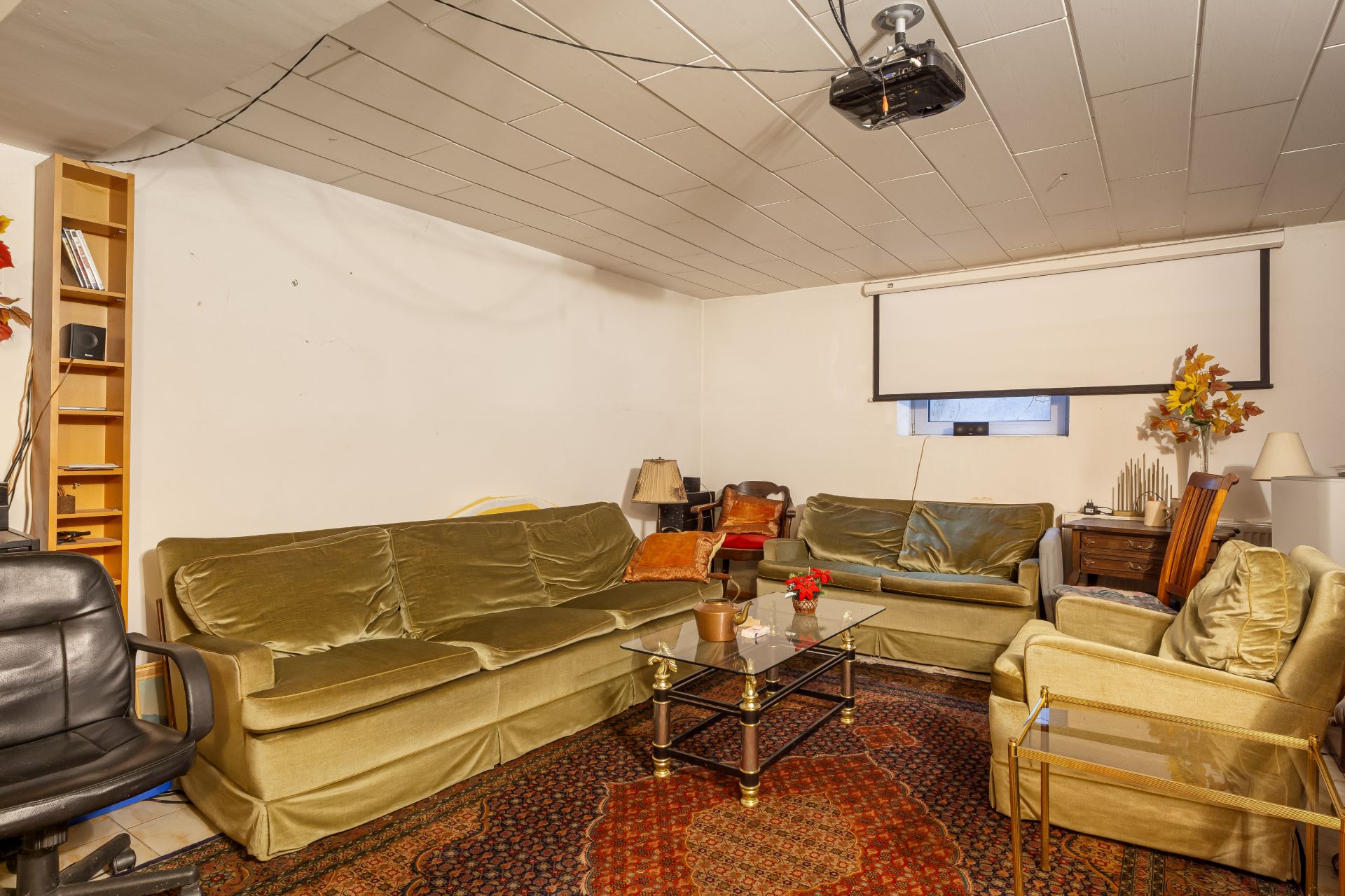 Wohnzimmer mit drei Sofas, Couchtisch, Teppichboden, Projektor und Leinwand an der Wand.
