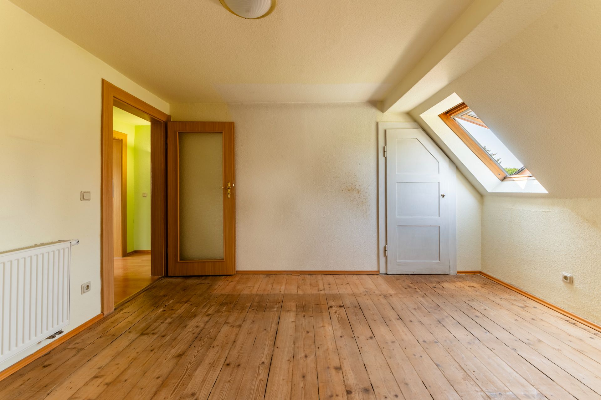 Leeres Zimmer mit Holzboden, offenem Fenster und zwei Türen, eine mit Glas, eine weiß.