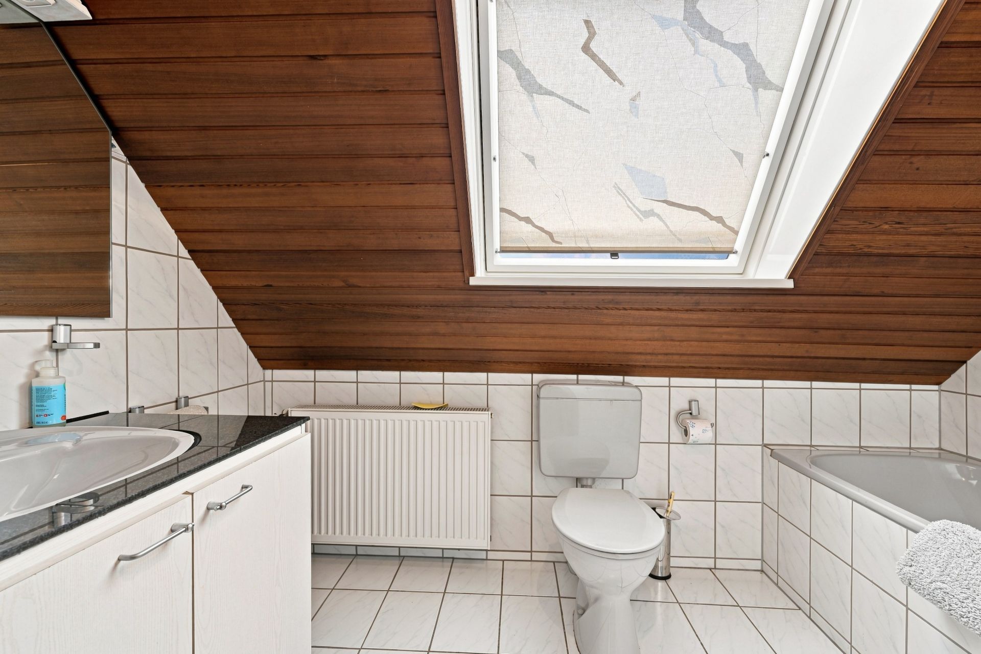 Helles Badezimmer mit Schrägdach, WC, Waschbecken, Badewanne und Fenster.