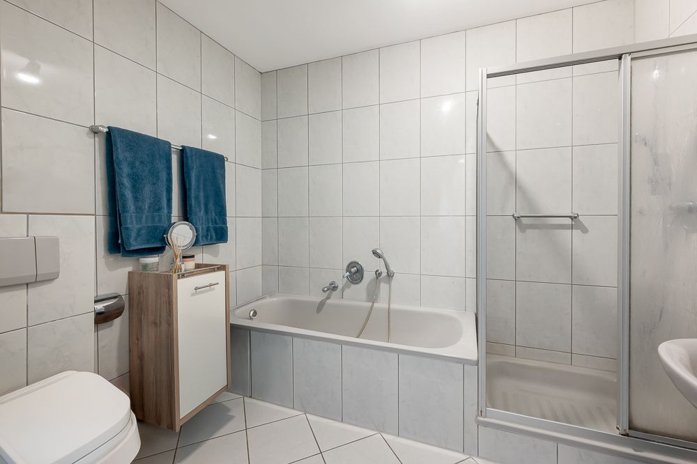 Helles Badezimmer mit Badewanne, Dusche, Toilette, Waschtisch und zwei blauen Handtüchern an der Wand.
