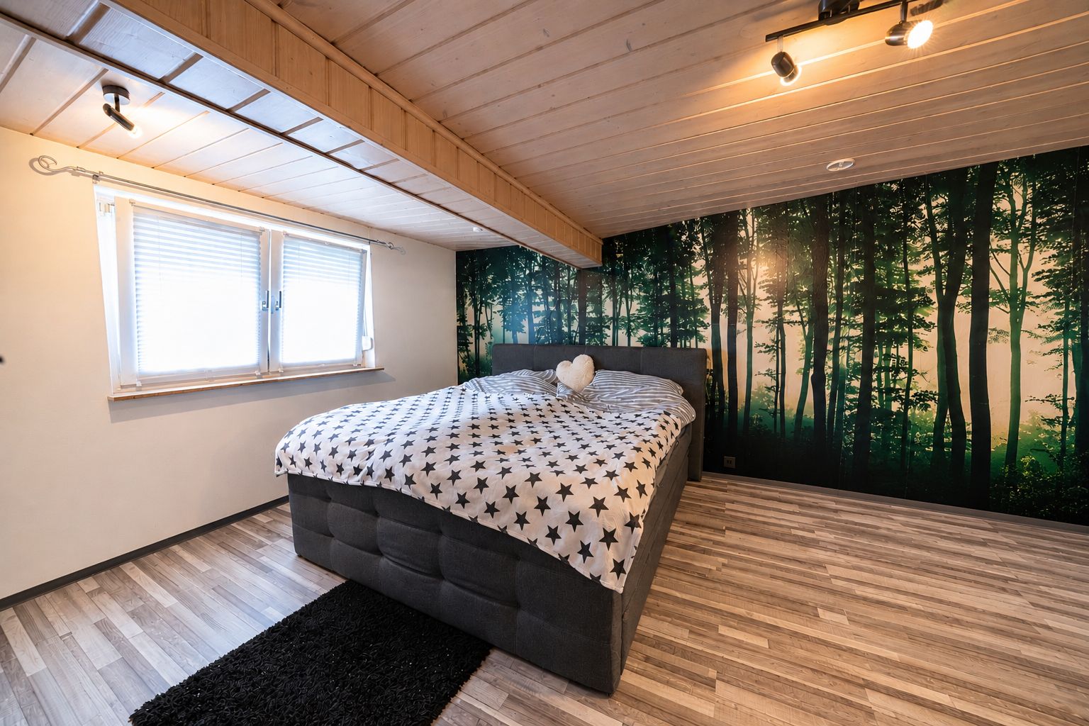 Schlafzimmer mit Doppelbett, Sternendecke und großen Fenstern, Wand mit Waldmotiv-Tapete.