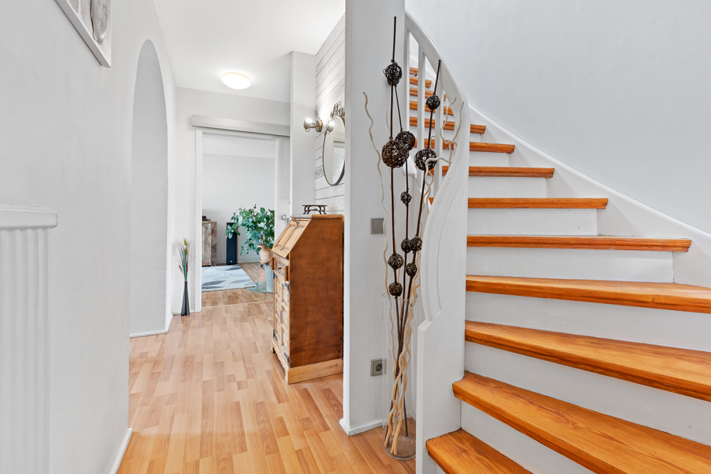 Heller Flur mit Holztreppe, Schreibtisch, Wandspiegel und Dekoration.