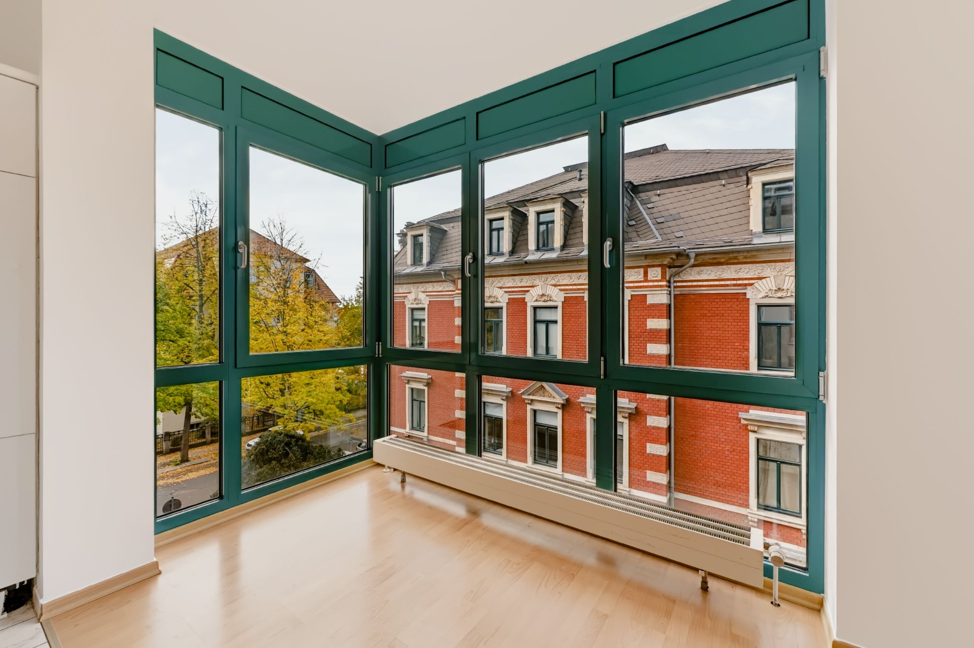 Heller Raum mit Eckfenster und Blick auf ein rotes Altbaugebäude.