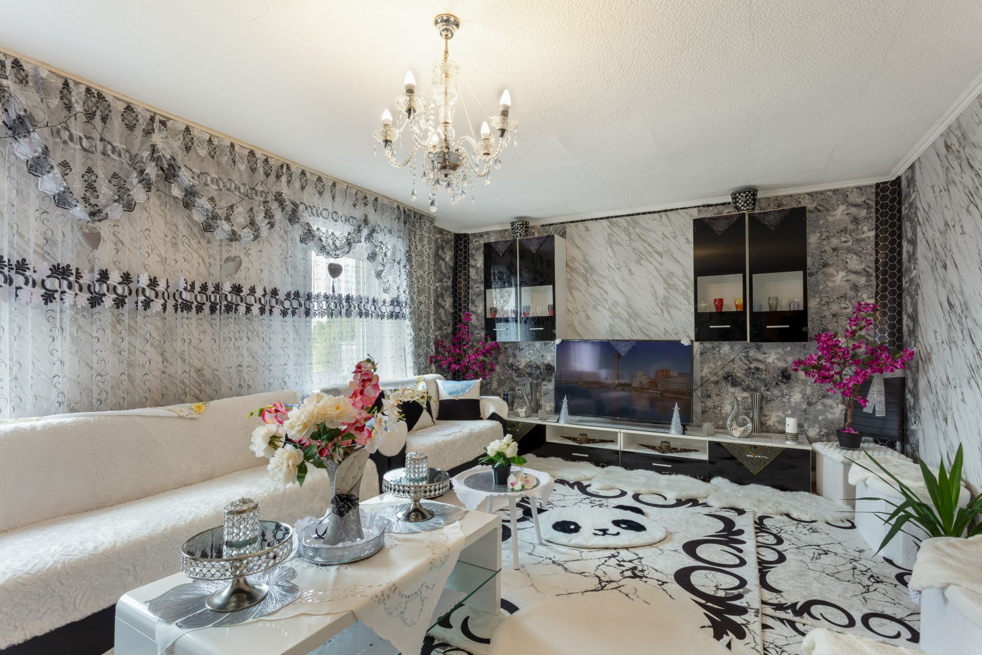 Wohnzimmer mit weißen Sofas, Blumen, Kronleuchter und gemustertem Teppich.