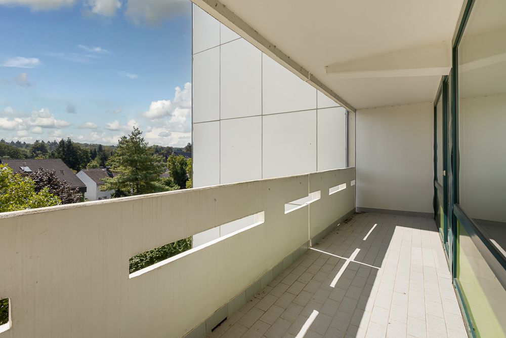 Überdachter Balkon mit Glasbrüstung und Blick auf Bäume und Wohnhäuser.