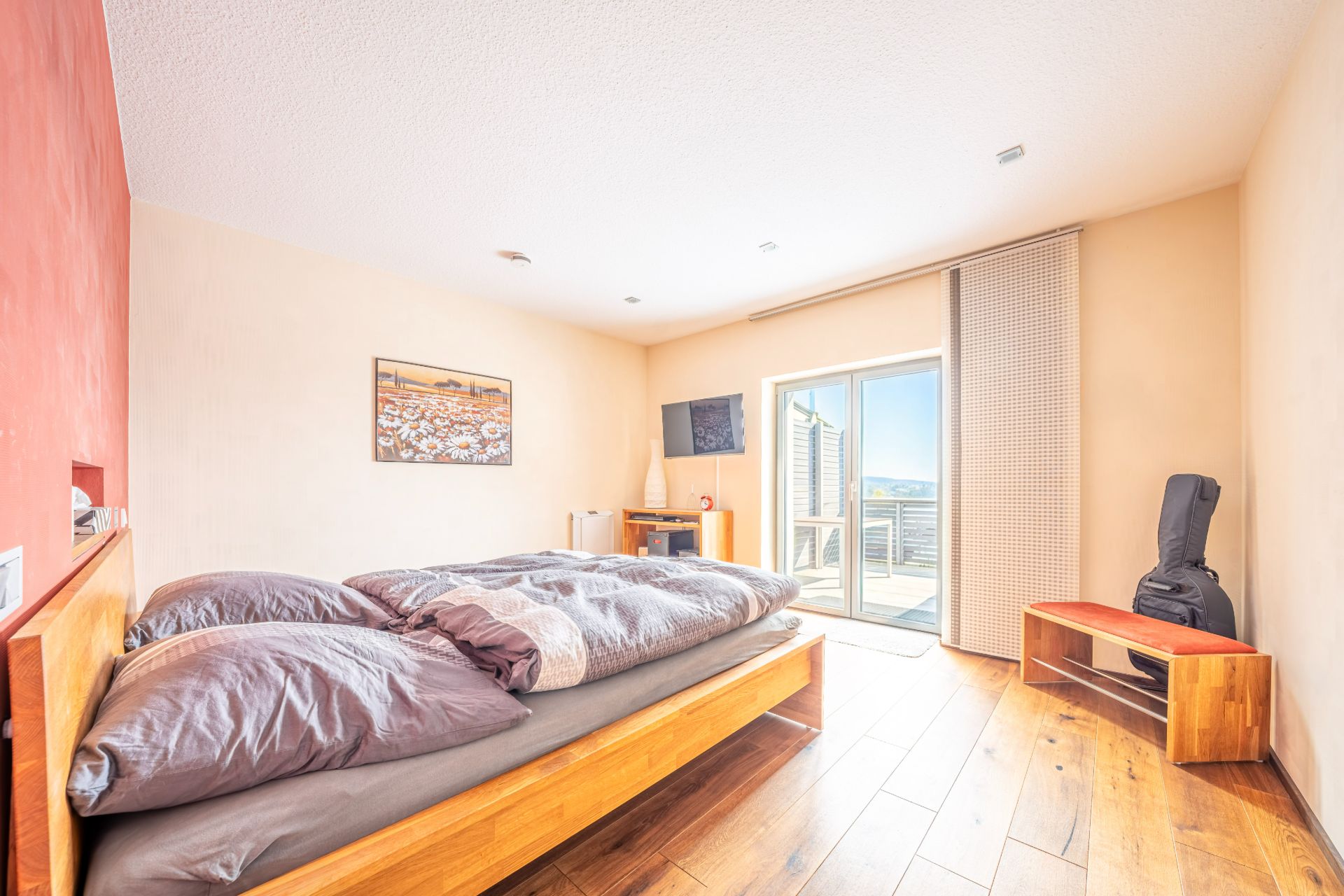 Helles Schlafzimmer mit Doppelbett, Holzfußboden, Balkonzugang und Gitarre in der Ecke.