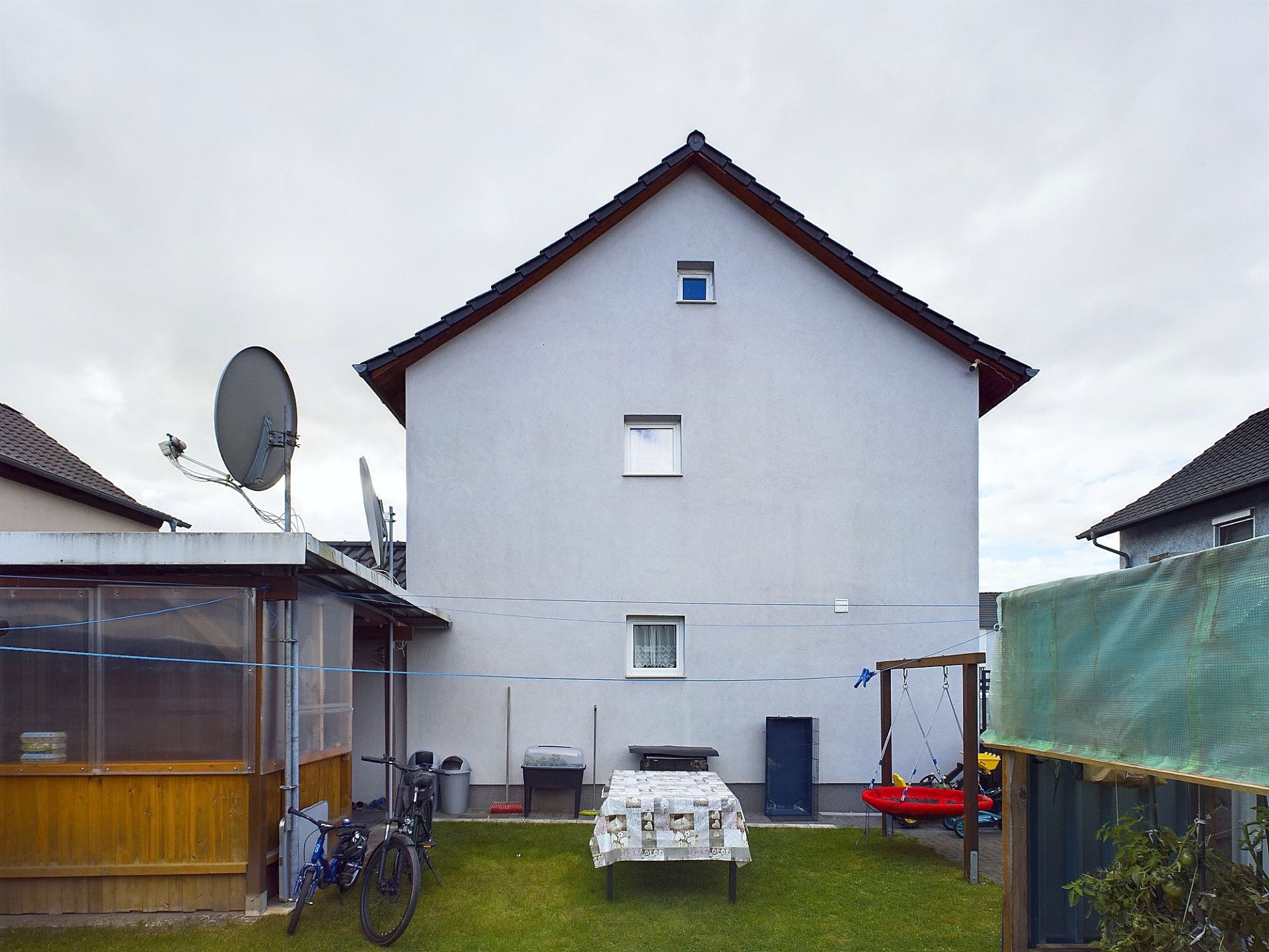 Rückseite eines Hauses mit Garten, einem Tisch, Schaukel und zwei Fahrrädern.