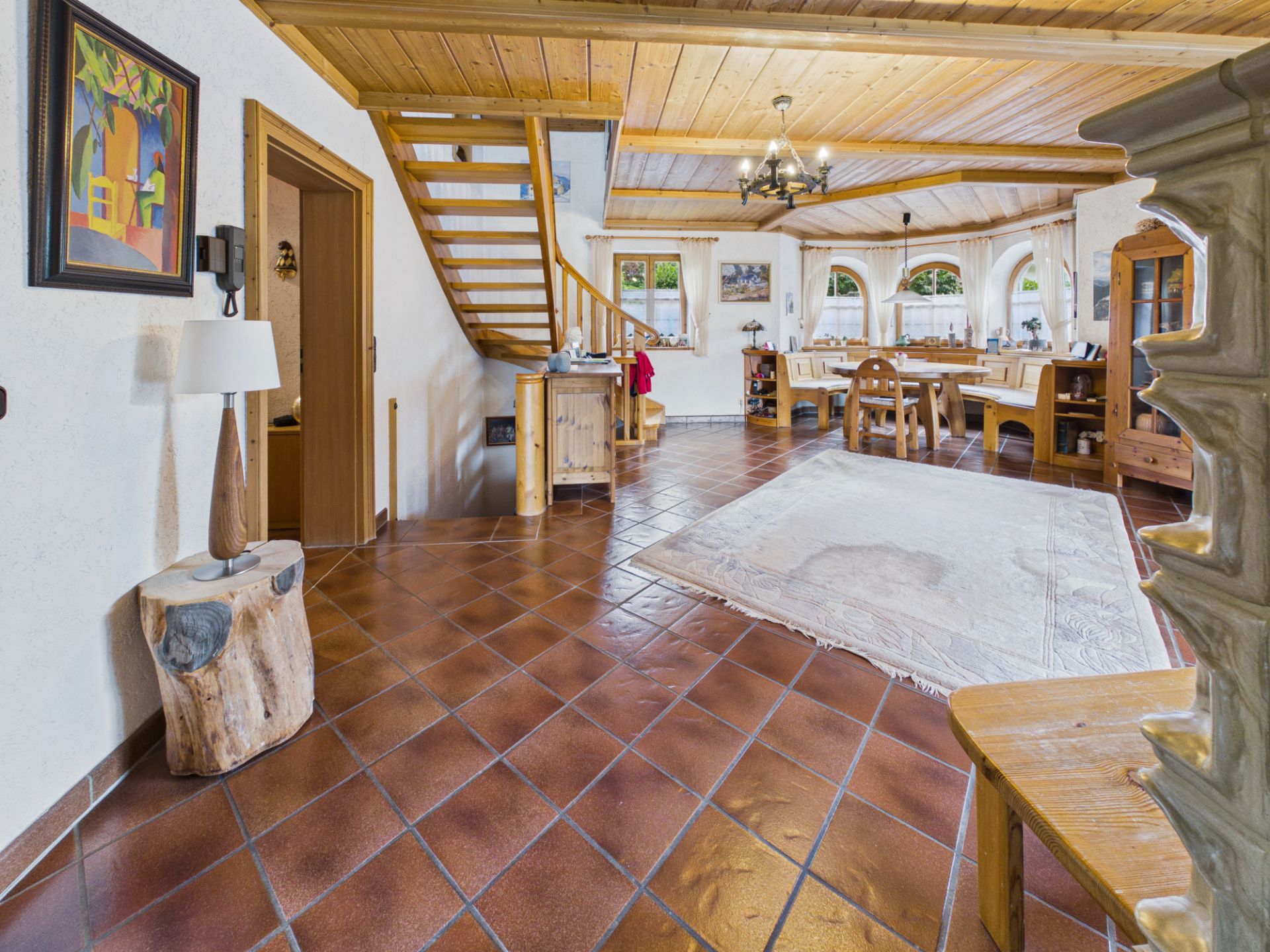 Helles Wohnzimmer mit Holzboden, Esstisch, Teppich, Treppe und großen Fenstern.