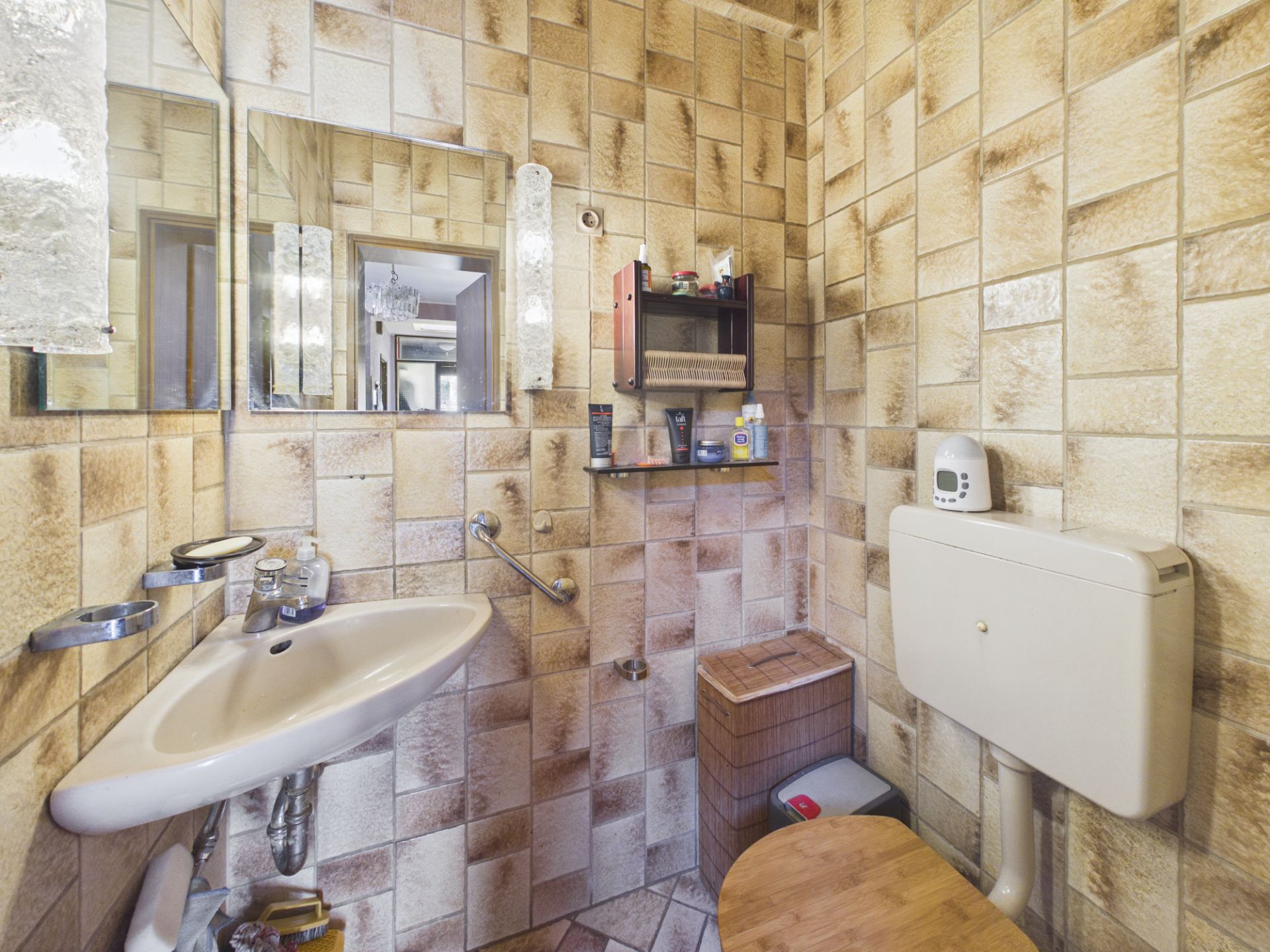 Kleines Badezimmer mit Wandfliesen, Waschbecken, Spiegel, Regal und Toilette.