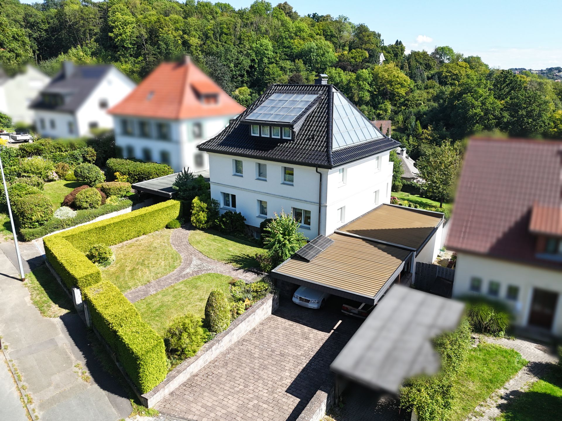 Weißes Einfamilienhaus mit Garten, Auffahrt und Carport in Wohngegend.