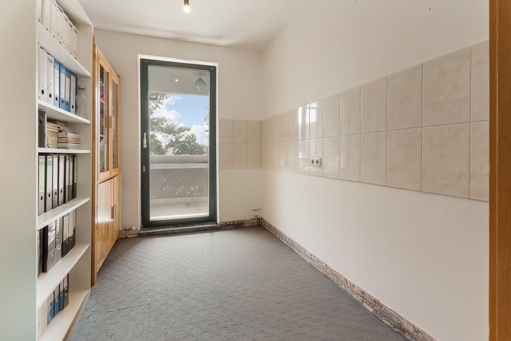 Kleiner Raum mit Regal, Glasschrank, Fliesen an einer Wand und Tür zum Balkon.