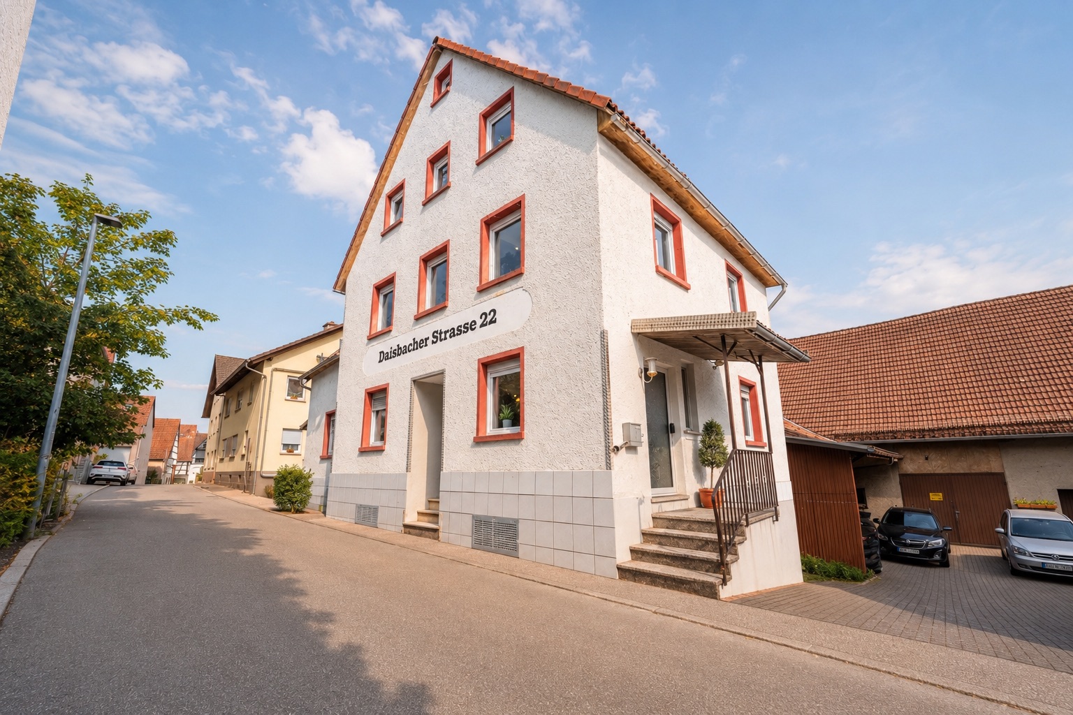 Wohnhaus mit weißer Fassade und roten Fensterrahmen an einer ruhigen Straße.