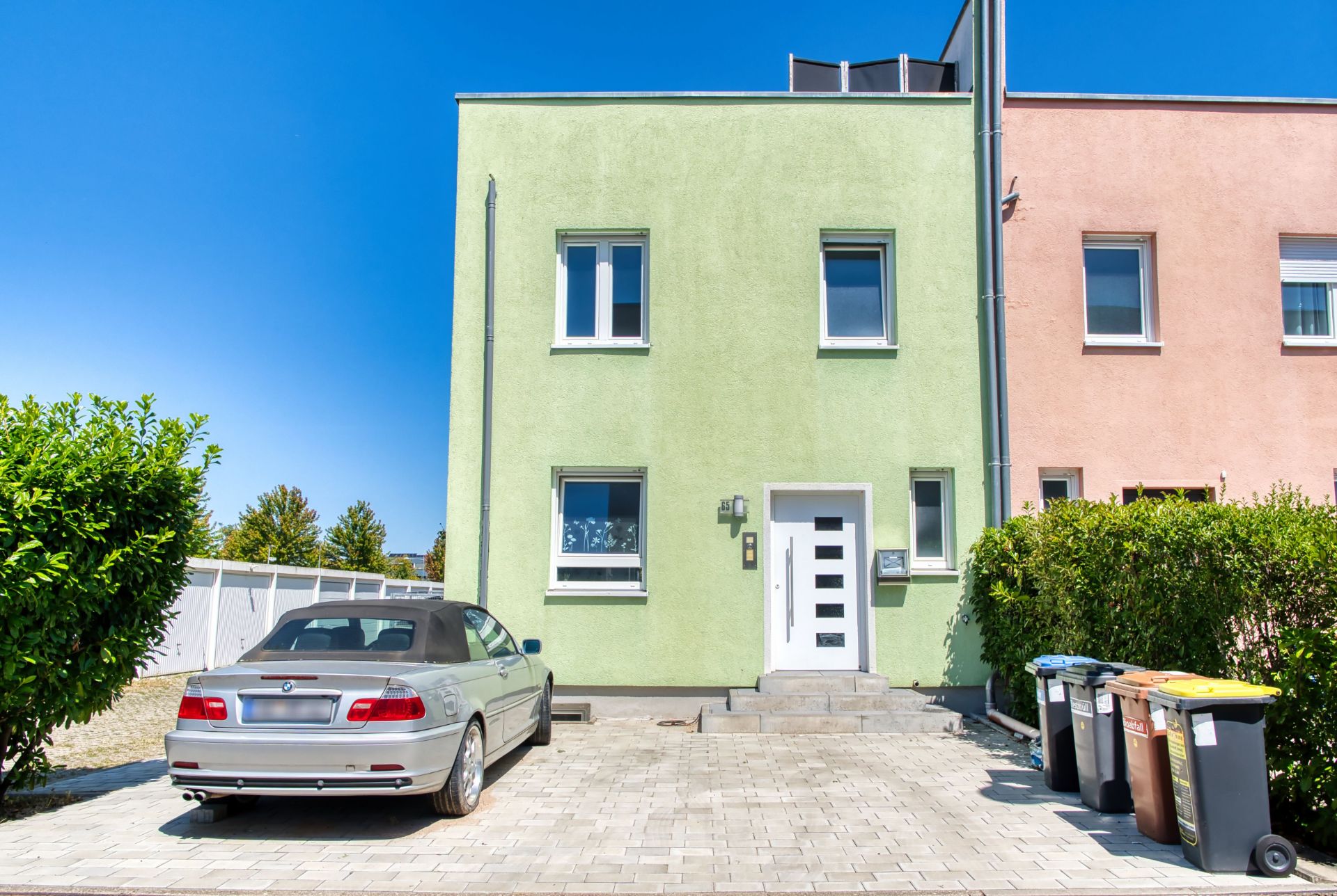 Grünes Wohnhaus mit Auto auf Einfahrt und Mülltonnen am rechten Rand.