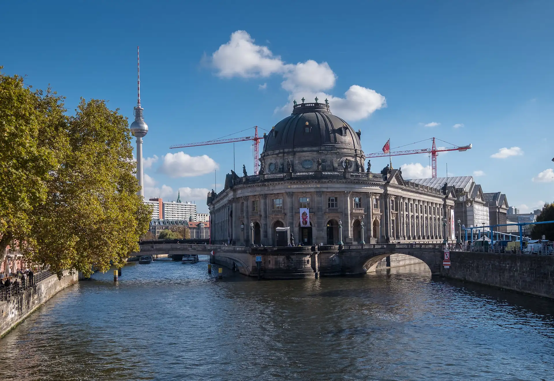 Großes historisches Gebäude mit Kuppel an einem Fluss, im Hintergrund Fernsehturm und Baukräne.