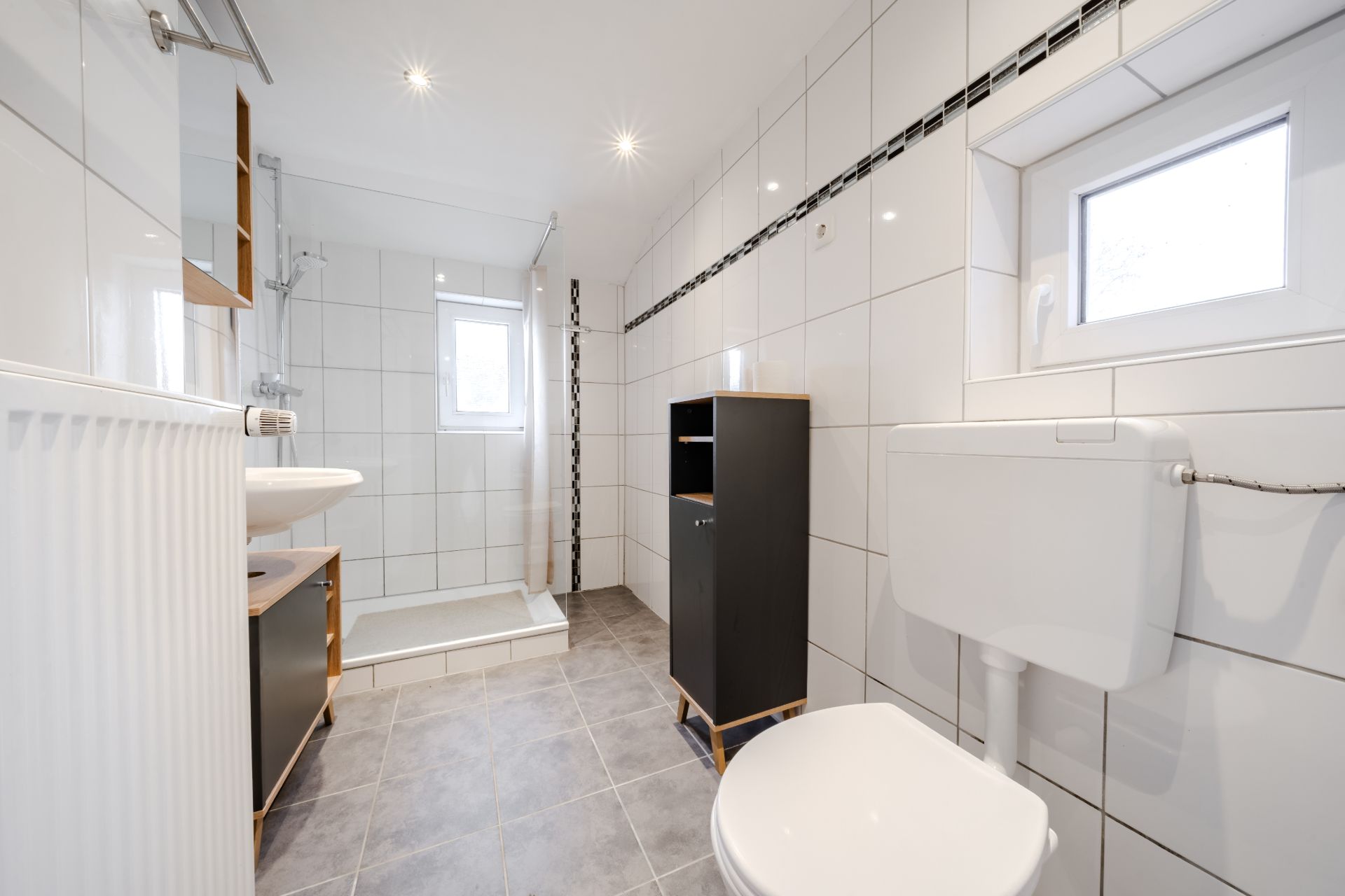 Modernes Badezimmer mit Dusche, Toilette, Waschbecken und kleinem Fenster.