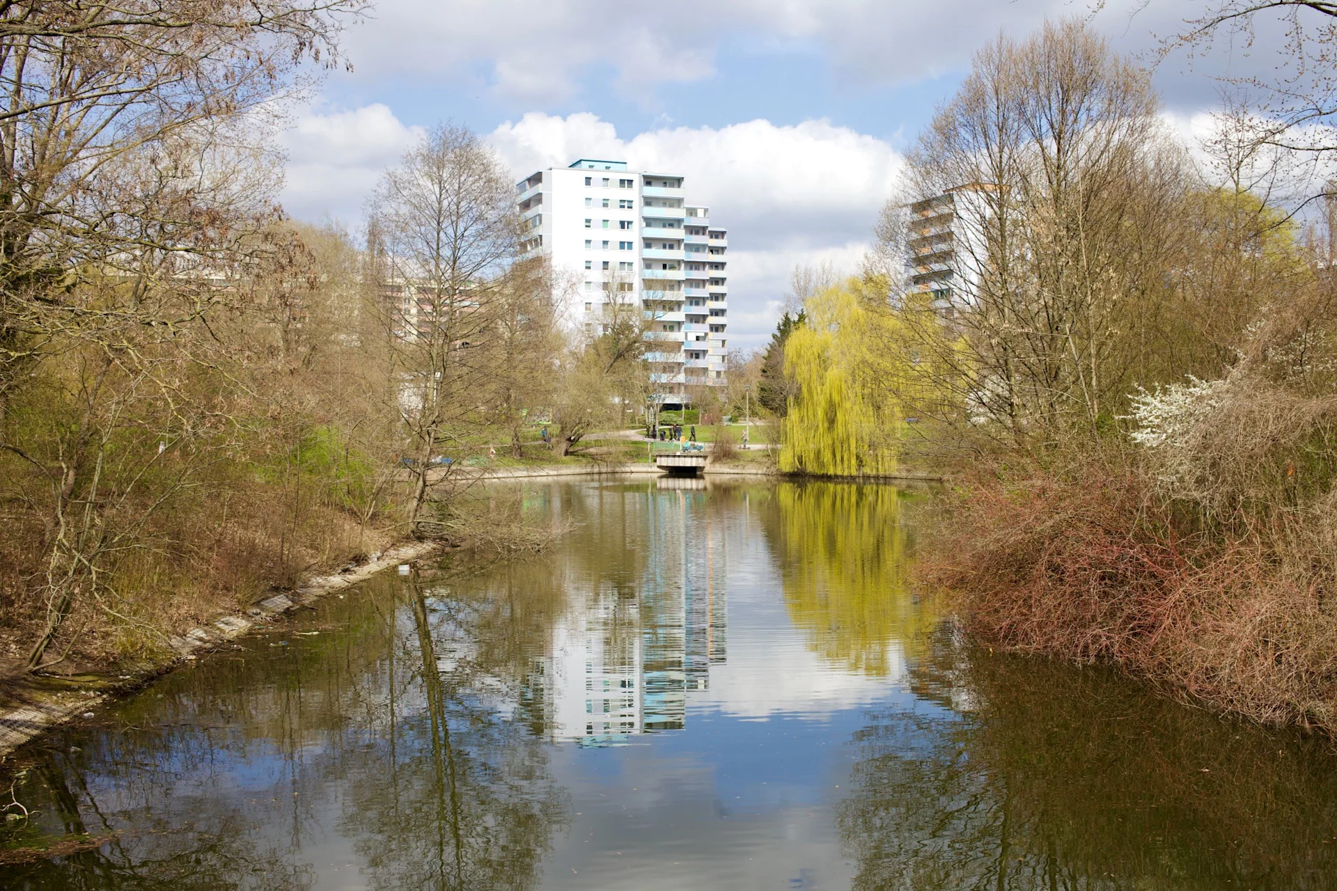 Wohngebäude hinter einem kleinen Teich mit Bäumen am Ufer.