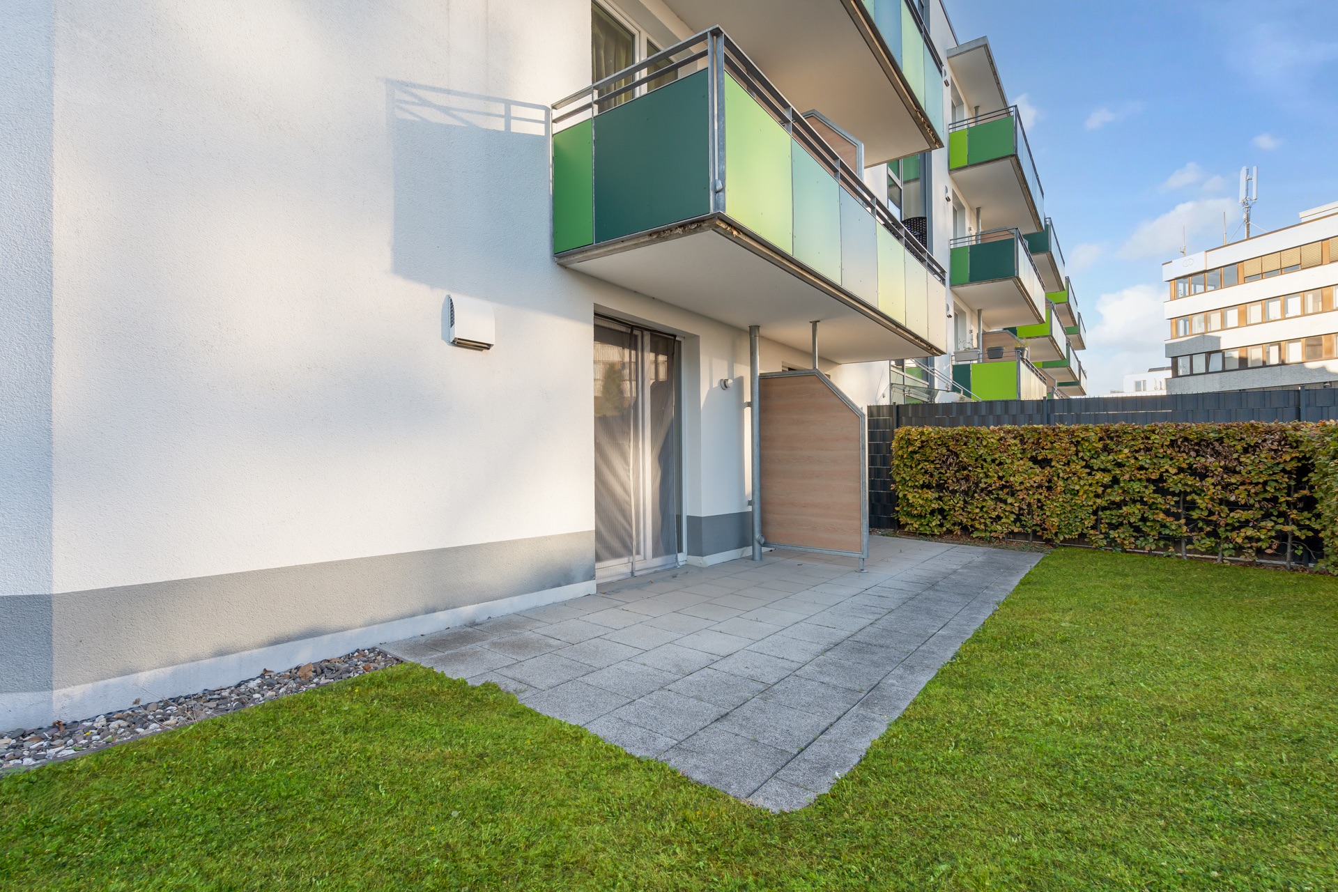 Gepflegte Terrasse mit Rasenfläche neben einem modernen Wohngebäude mit Balkonen.
