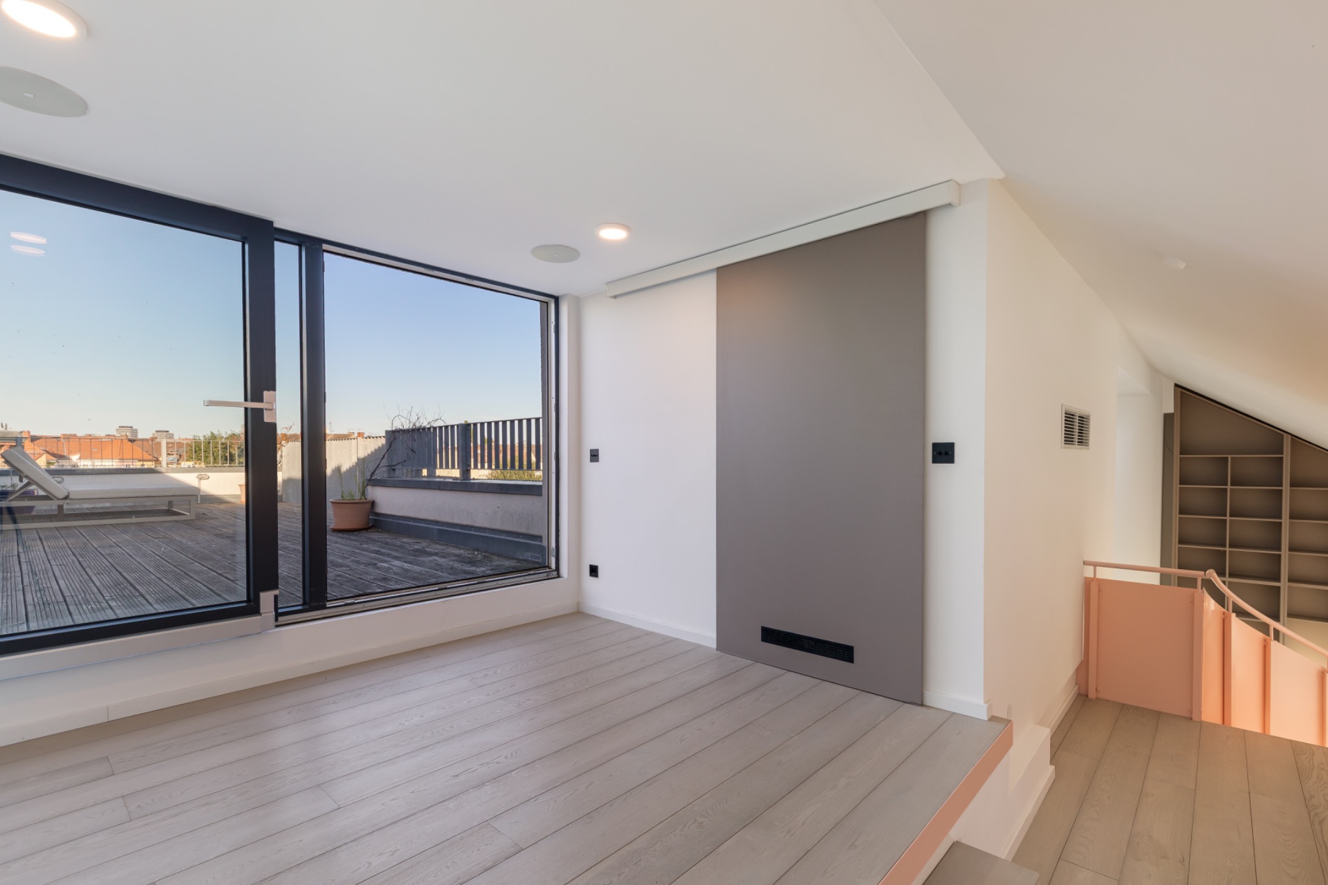 Heller Raum mit Holzboden, großen Fenstern und Zugang zu einer Dachterrasse.