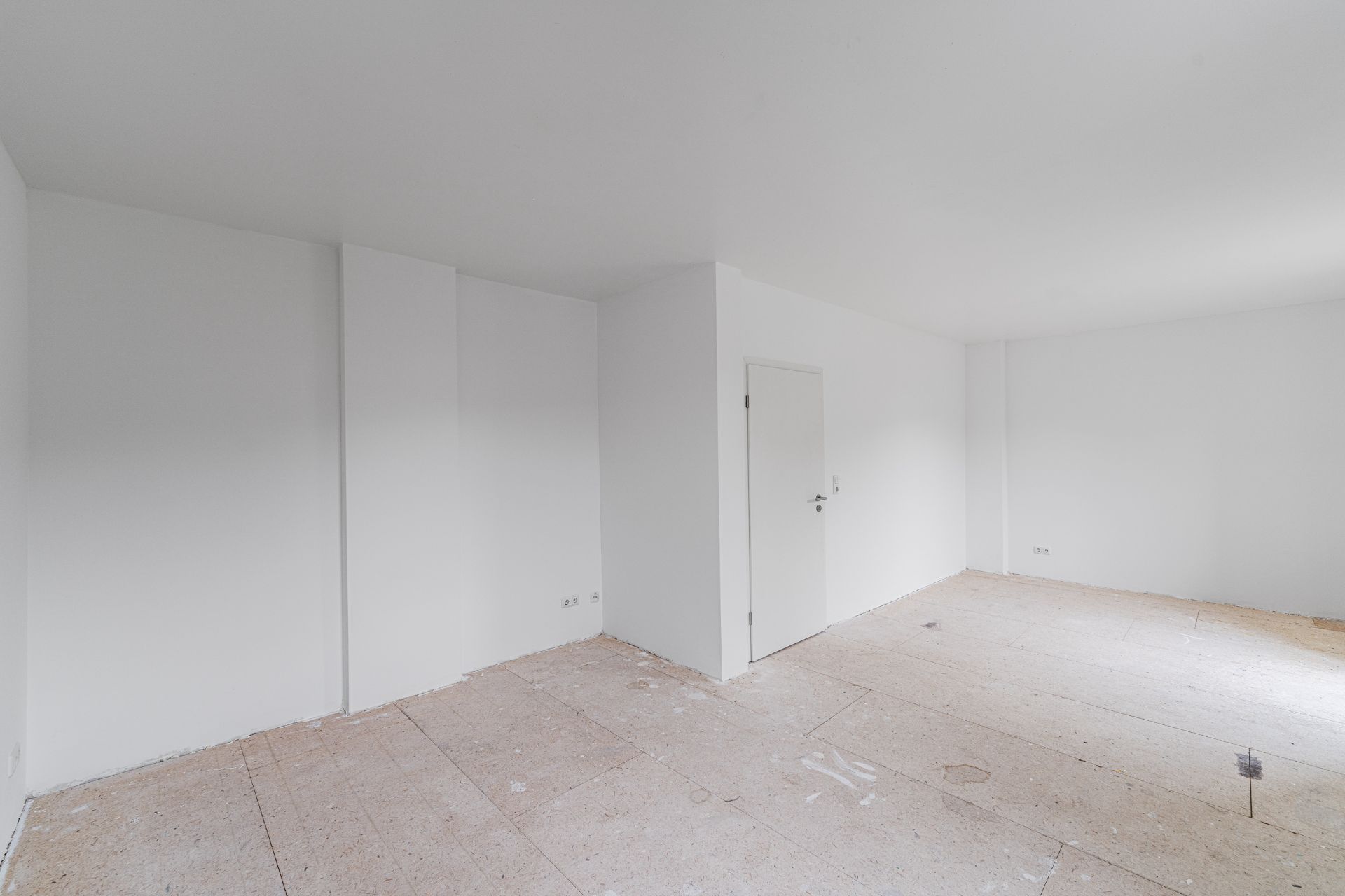 Leerer, weiß gestrichener Raum mit einer Tür und unfertigem Fußboden.