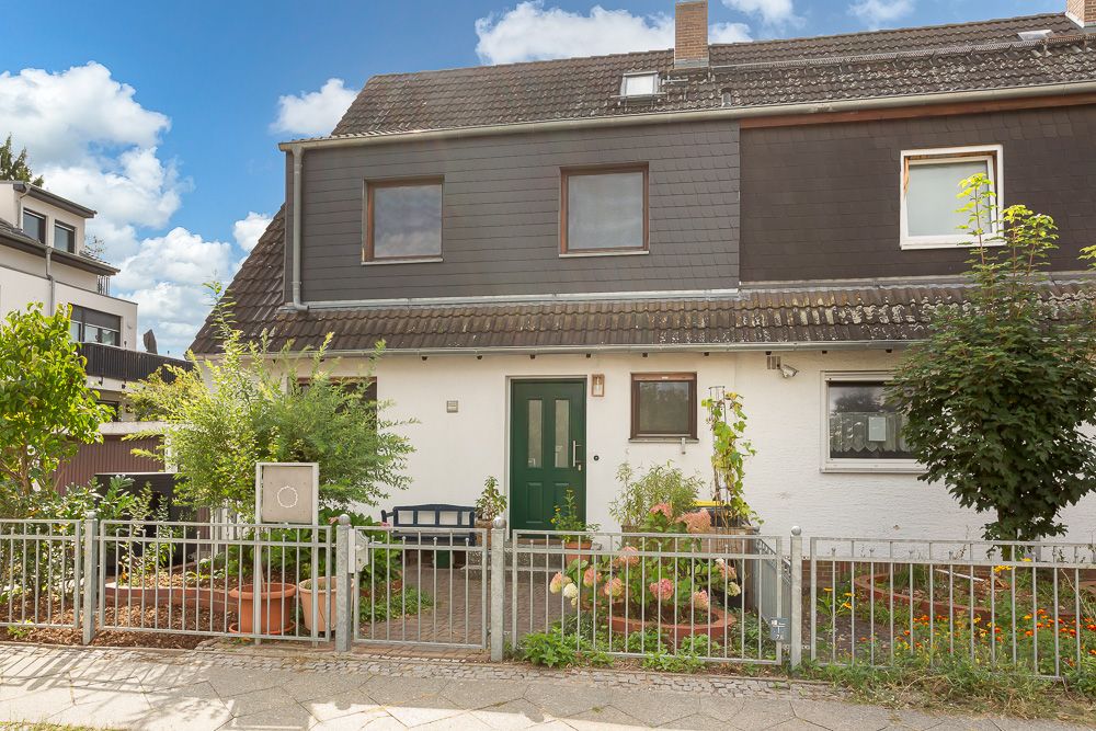 Vorderansicht eines zweistöckigen Wohnhauses mit Garten und grünem Zaun.