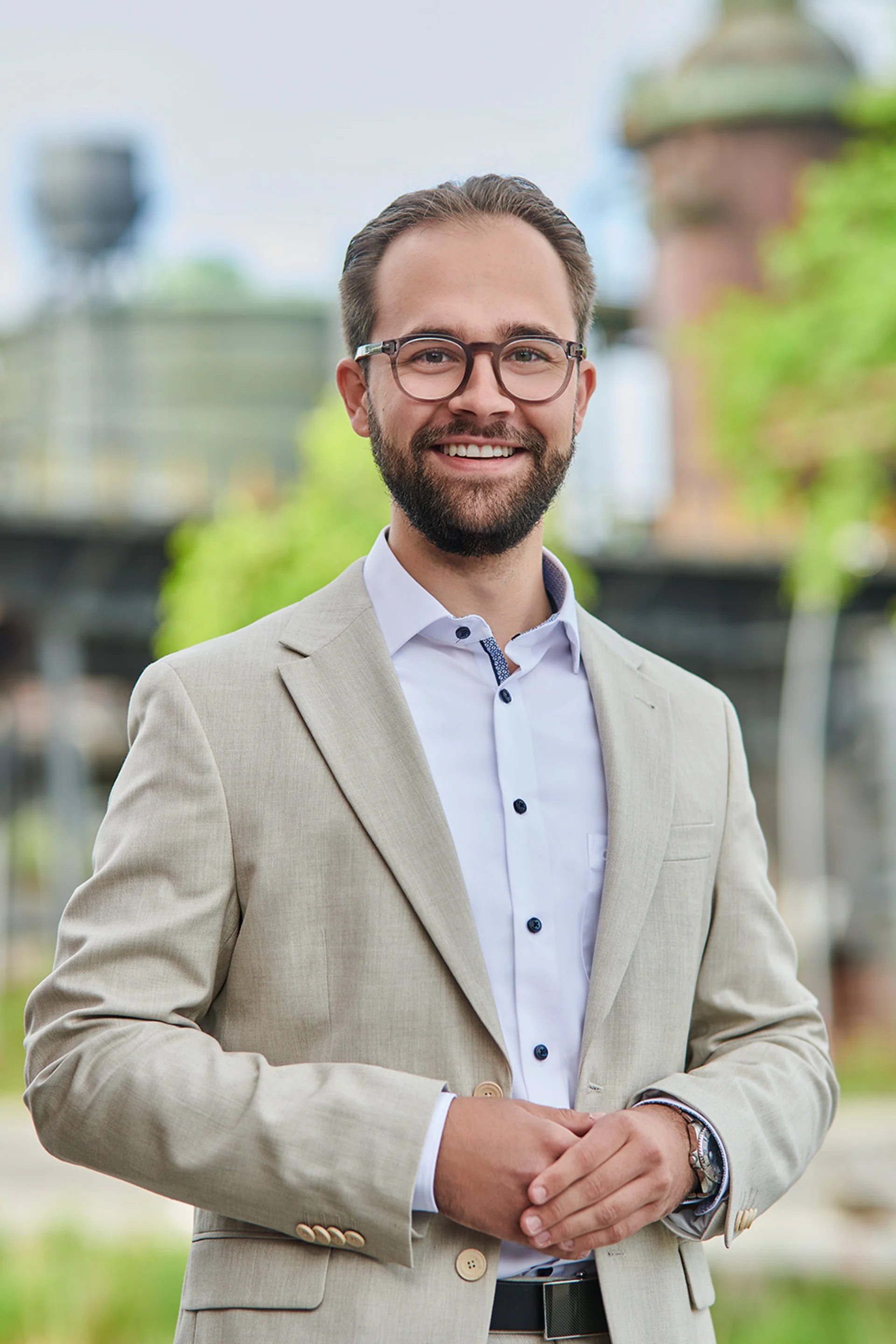 Mann mit Brille und weißem Hemd steht in einem hellen Flur mit Pflanzen im Hintergrund.