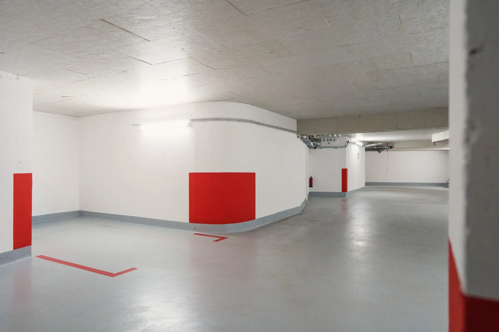 Leere Tiefgarage mit weiß gestrichenen Wänden und roten Markierungen.