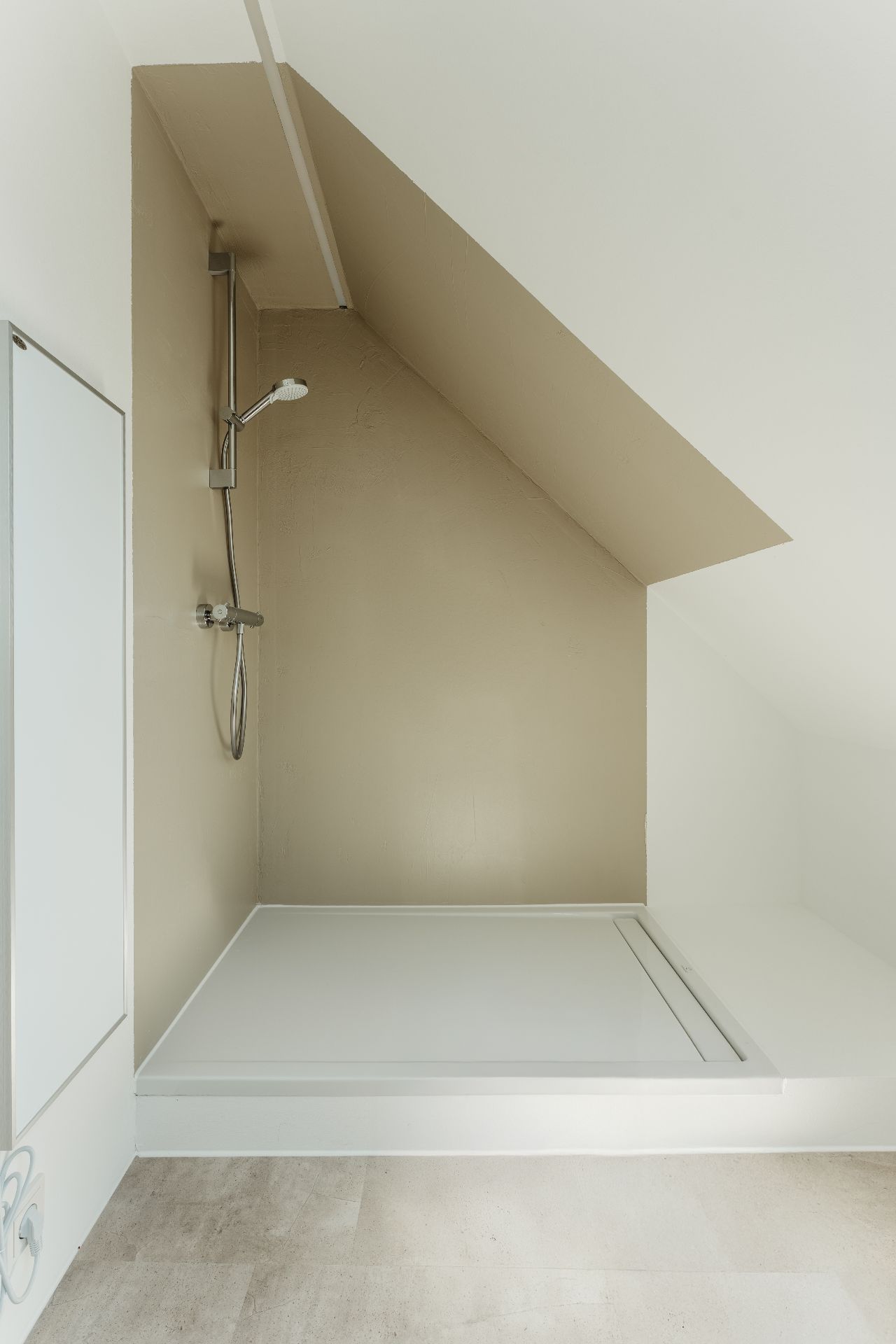Dusche mit schräger Decke und heller Wand in einem Badezimmer.