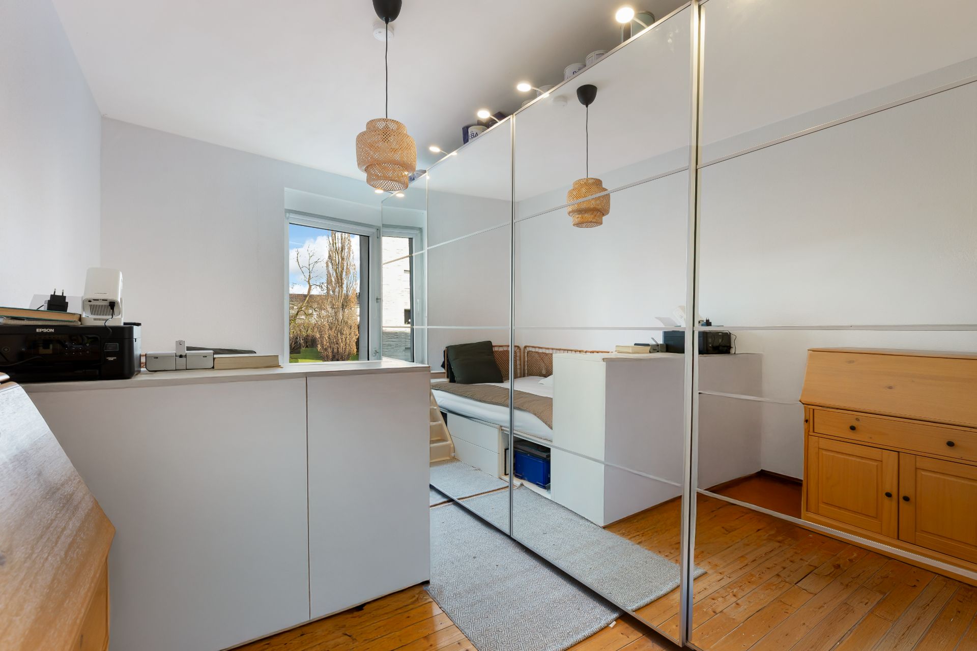 Helles Zimmer mit Spiegel-Schiebetüren, Sofa, Schreibtisch und Holzboden.