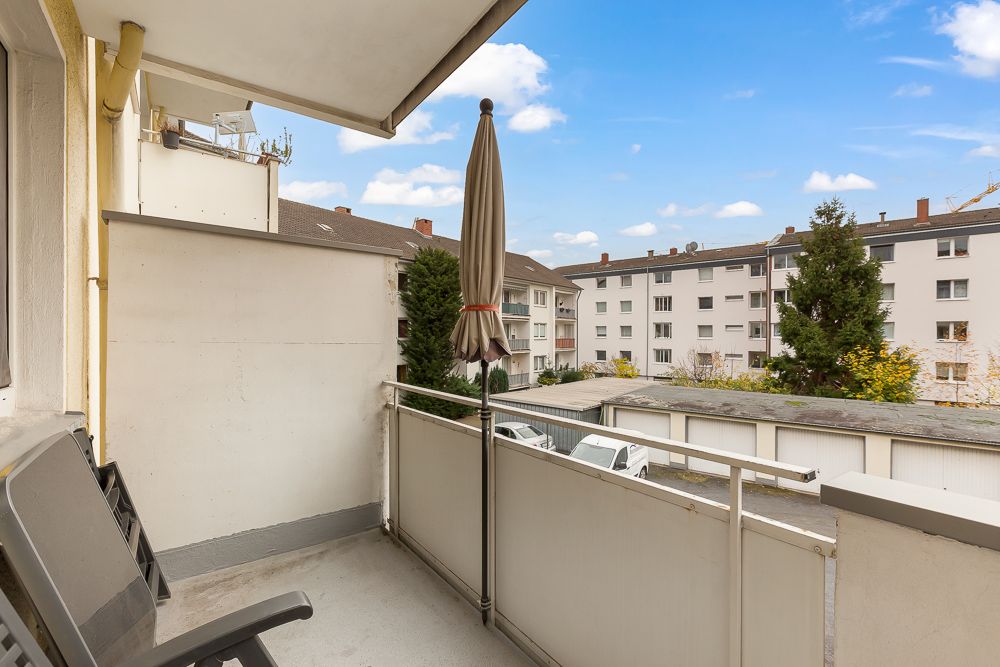 Balkon mit geschlossenem Sonnenschirm, zwei Stühlen und Blick auf Wohnhäuser.