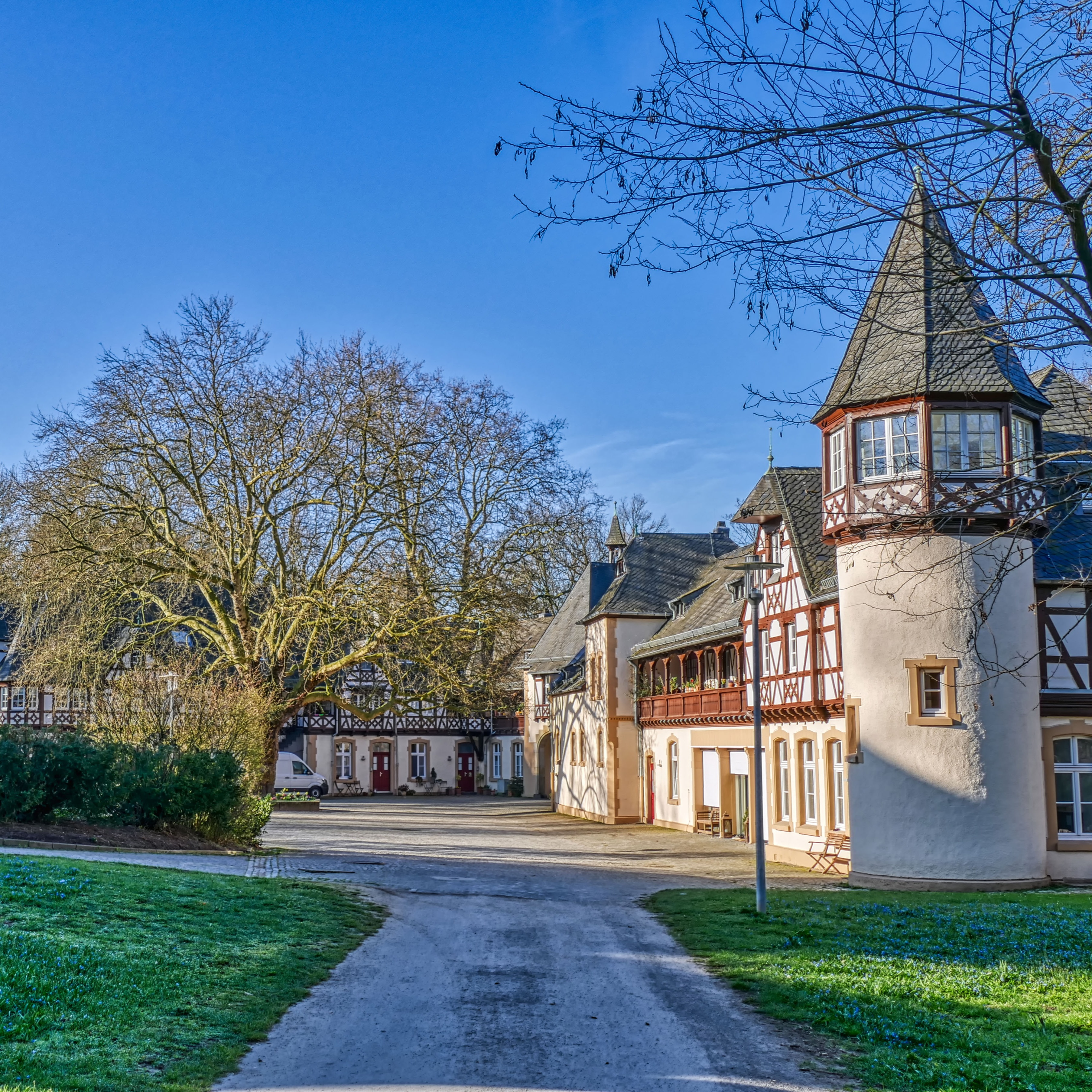 Historisches Wohngebäude mit Fachwerk und Rundturm, umgeben von Bäumen und Weg.