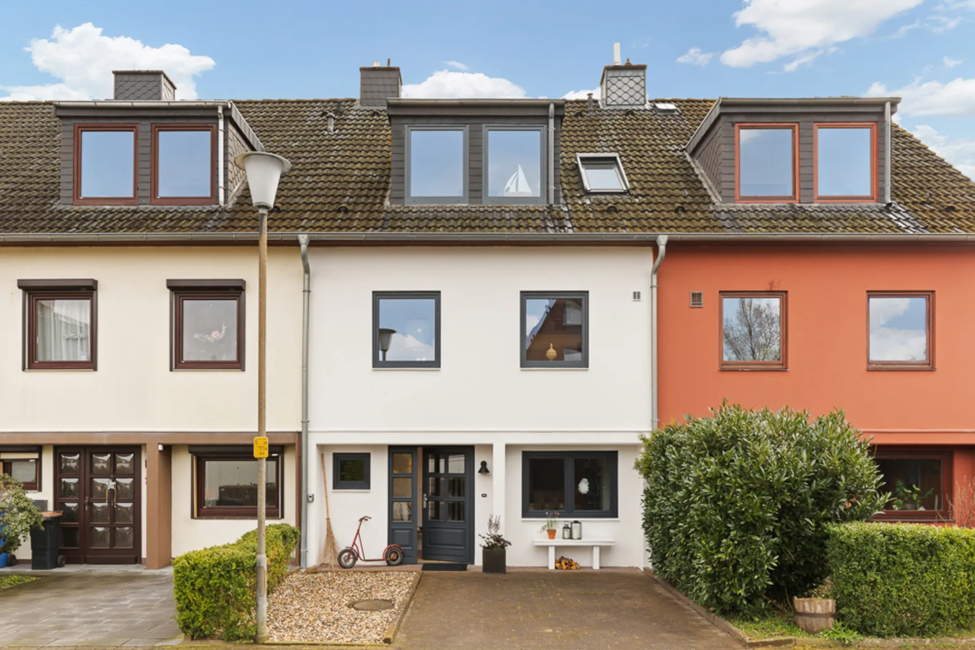 Vorderseite eines Reihenhauses mit weißer Fassade und drei Fenstern, kleiner Vorgarten.