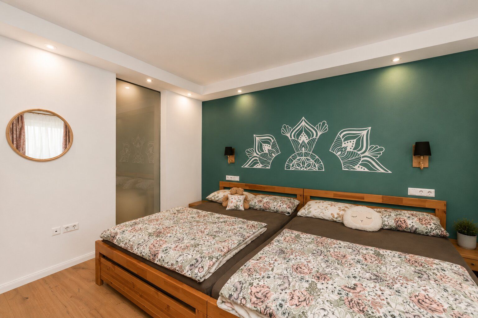 Schlafzimmer mit zwei Betten, gemusterten Bettdecken und grüner Wand mit weißen Dekorzeichnungen.