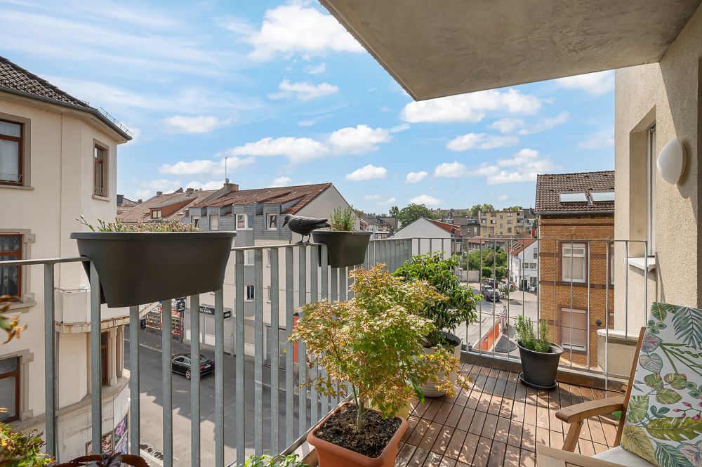 Balkon mit Pflanzen in Töpfen, Stuhl und Blick auf eine Wohnstraße bei Tageslicht.