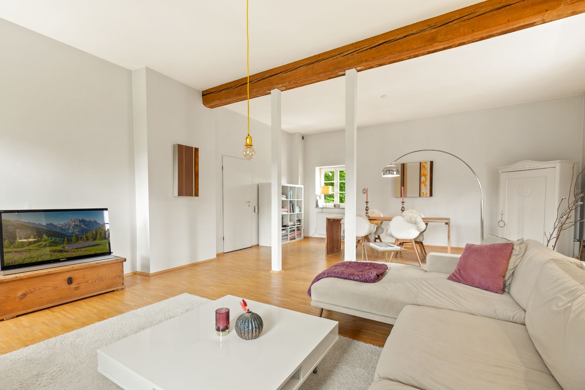 Modernes Wohnzimmer mit weißem Sofa, Couchtisch, Fernseher und Esstisch im Hintergrund.