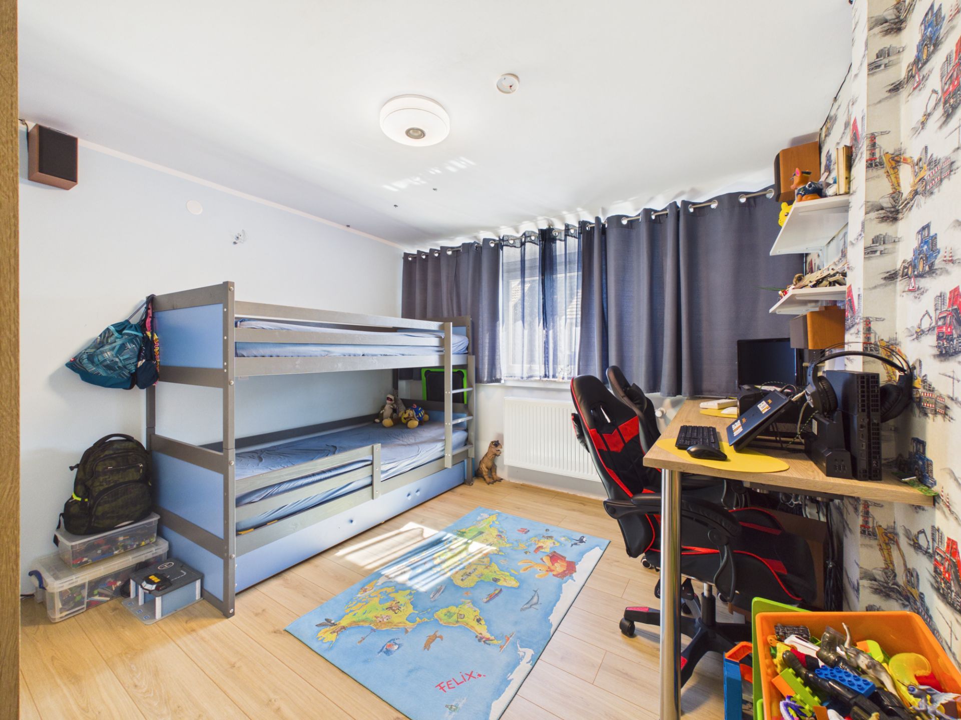 Kinderzimmer mit Etagenbett, Schreibtisch, Weltkarte-Teppich und Spielsachen.