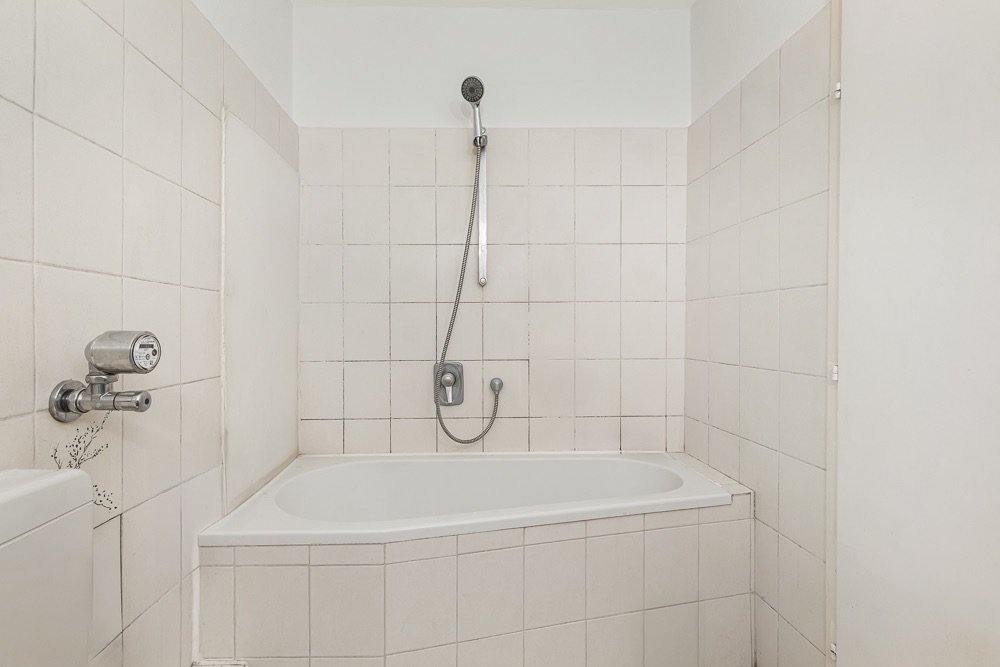Weiße Badewanne mit Duschkopf und beige gefliesten Wänden in einem Badezimmer.