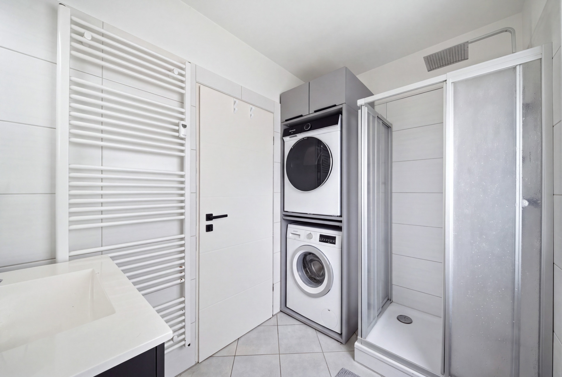 Modernes Badezimmer mit Dusche, Waschbecken, Heizkörper und gestapelter Waschmaschine und Trockner.