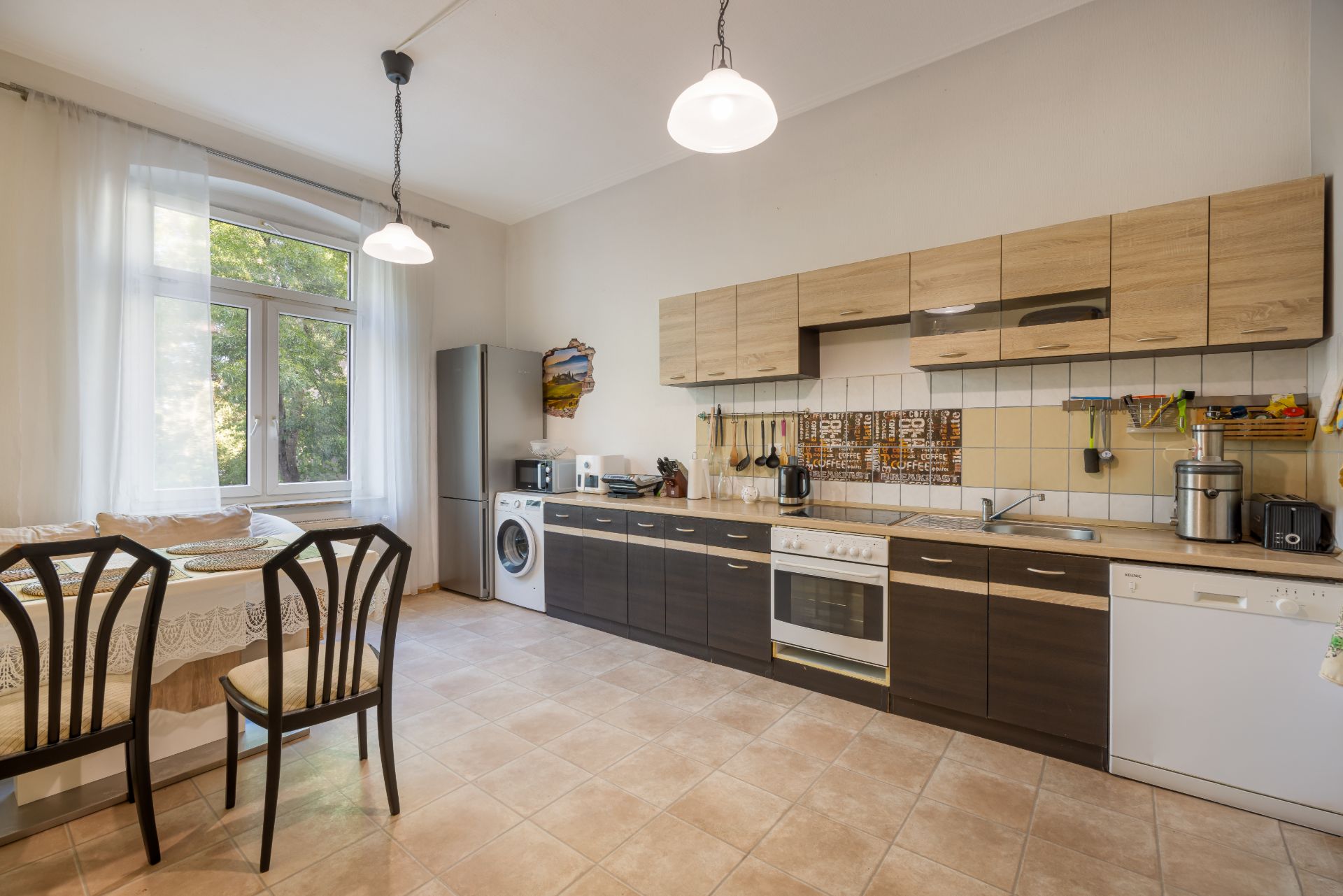 Moderne Wohnküche mit Esstisch, Stühlen, großen Fenstern und Küchenzeile mit Geräten.