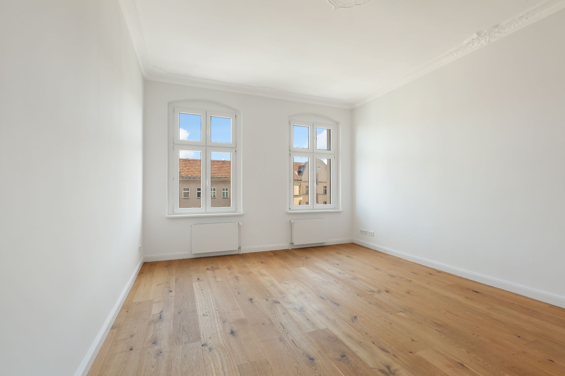 Heller, leerer Raum mit zwei großen Fenstern und Holzfußboden.