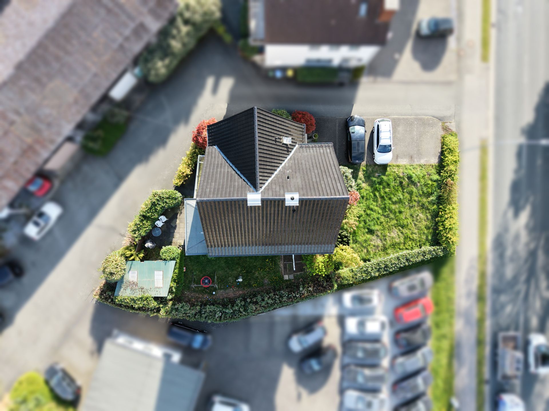 Luftaufnahme eines Einfamilienhauses mit Garten, Zufahrt und geparkten Autos.